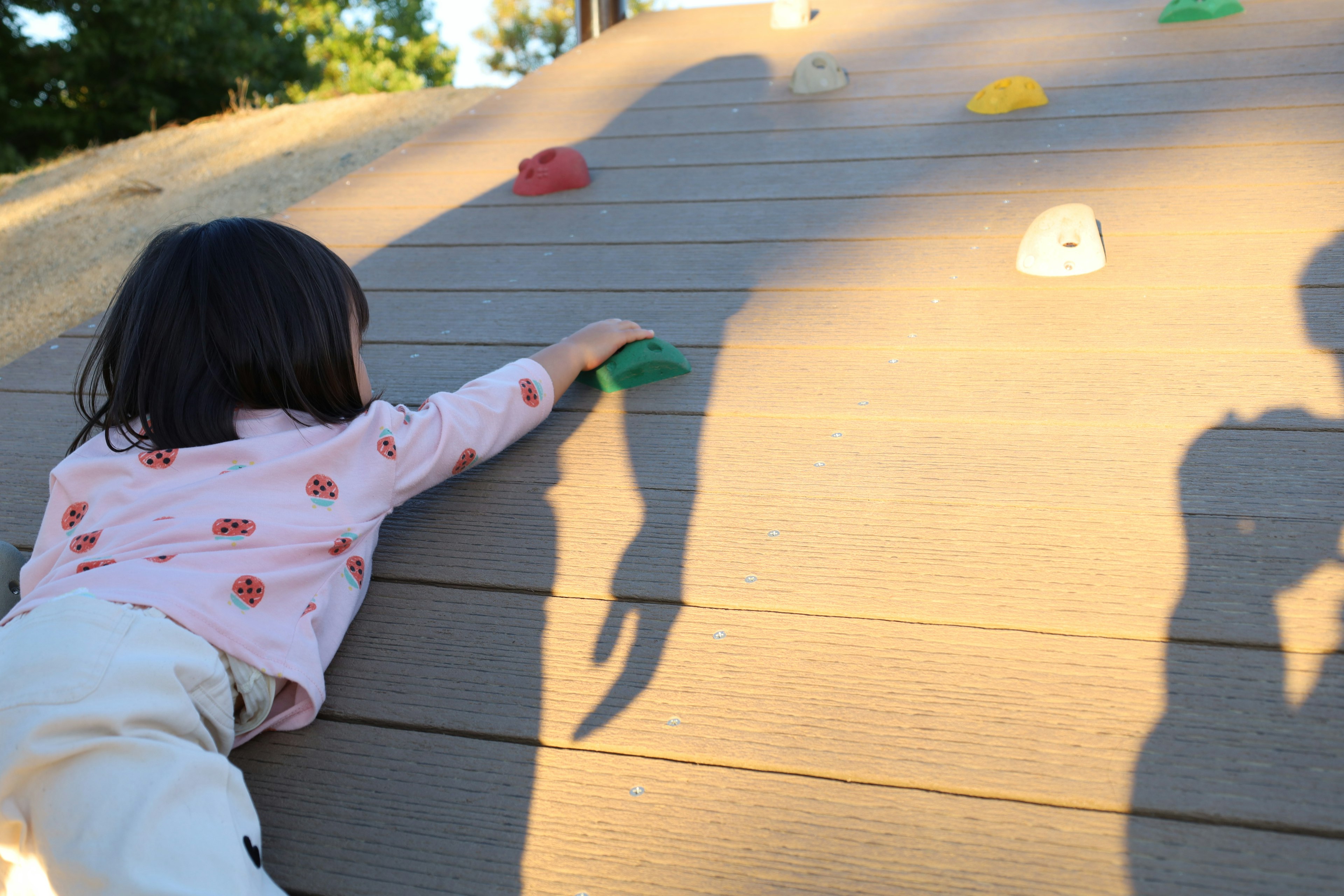 Child climbing on playground equipment with colorful holds and shadows