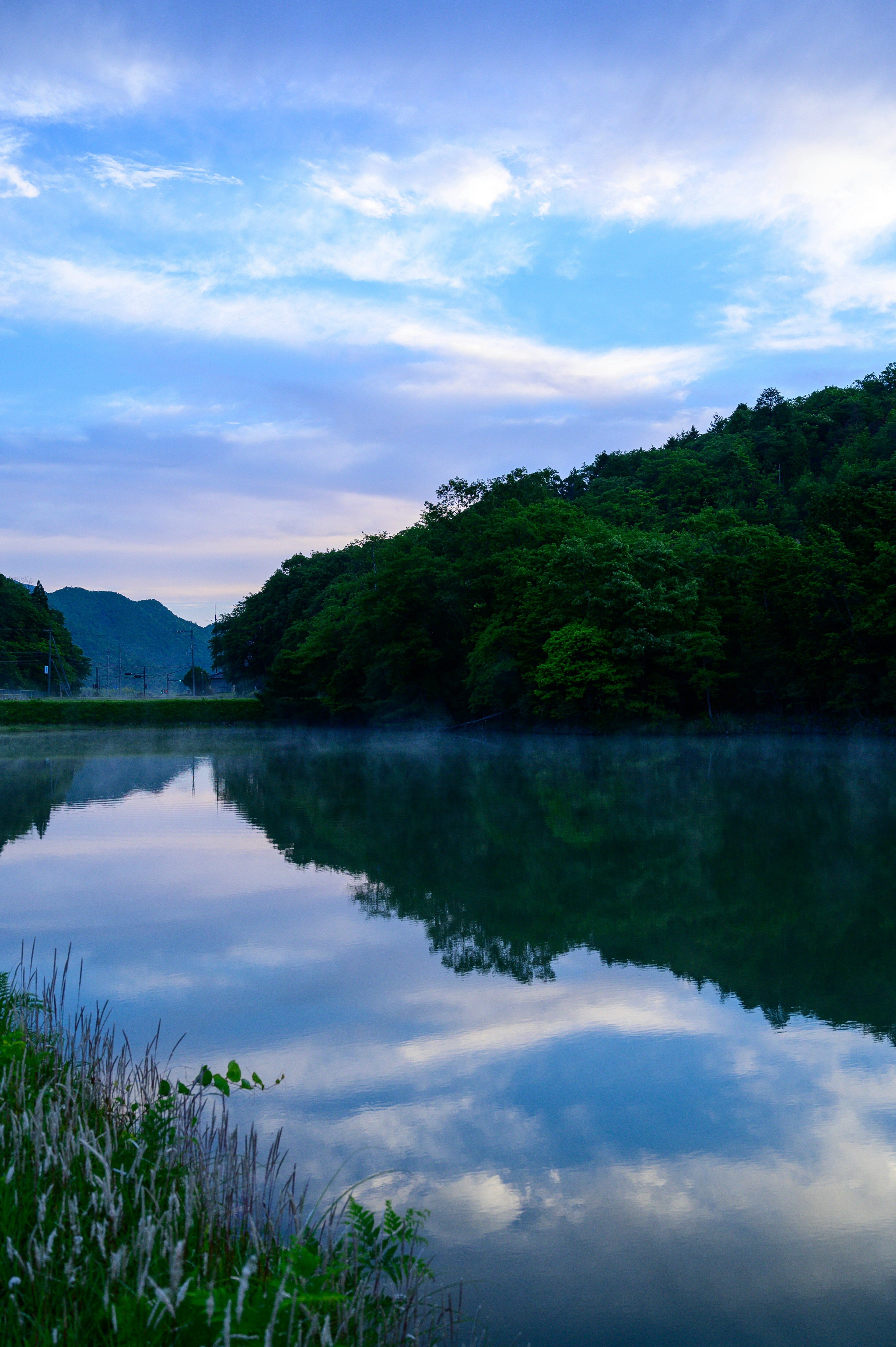 Danau tenang yang memantulkan langit biru dan gunung hijau