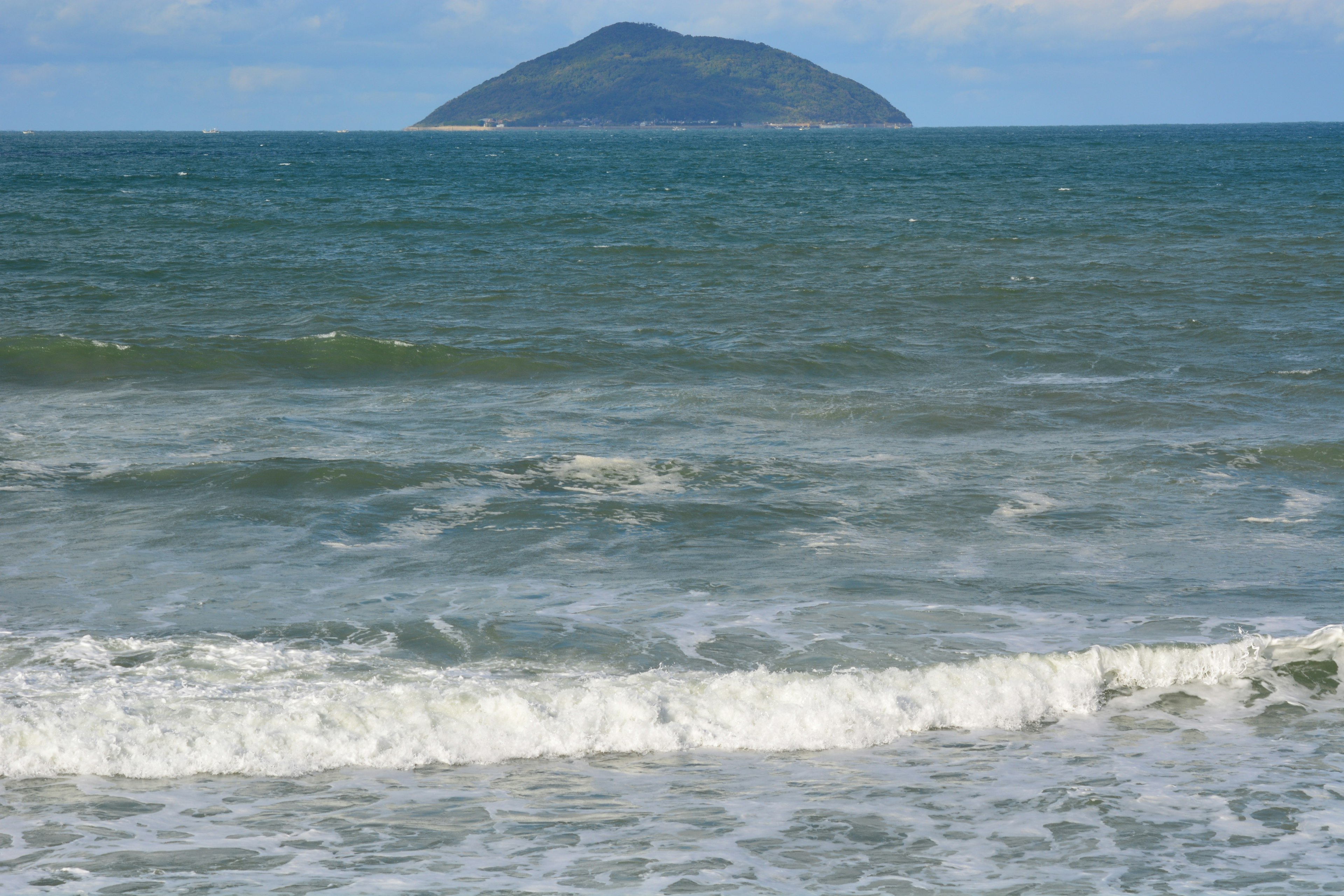 Vue panoramique de vagues océaniques bleues s'écrasant sur une plage avec une petite île au loin