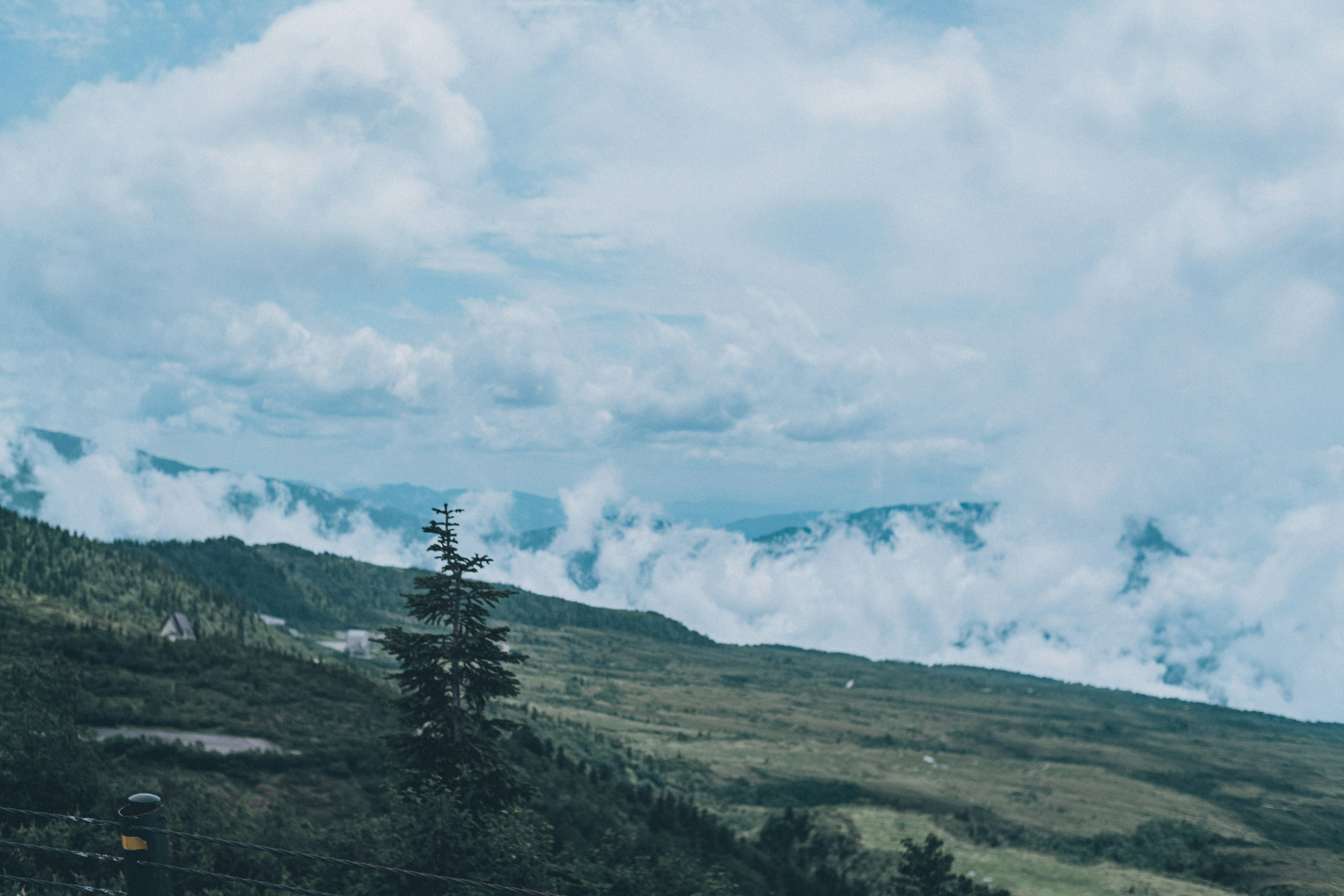 青い空と雲に覆われた緑豊かな山々の風景