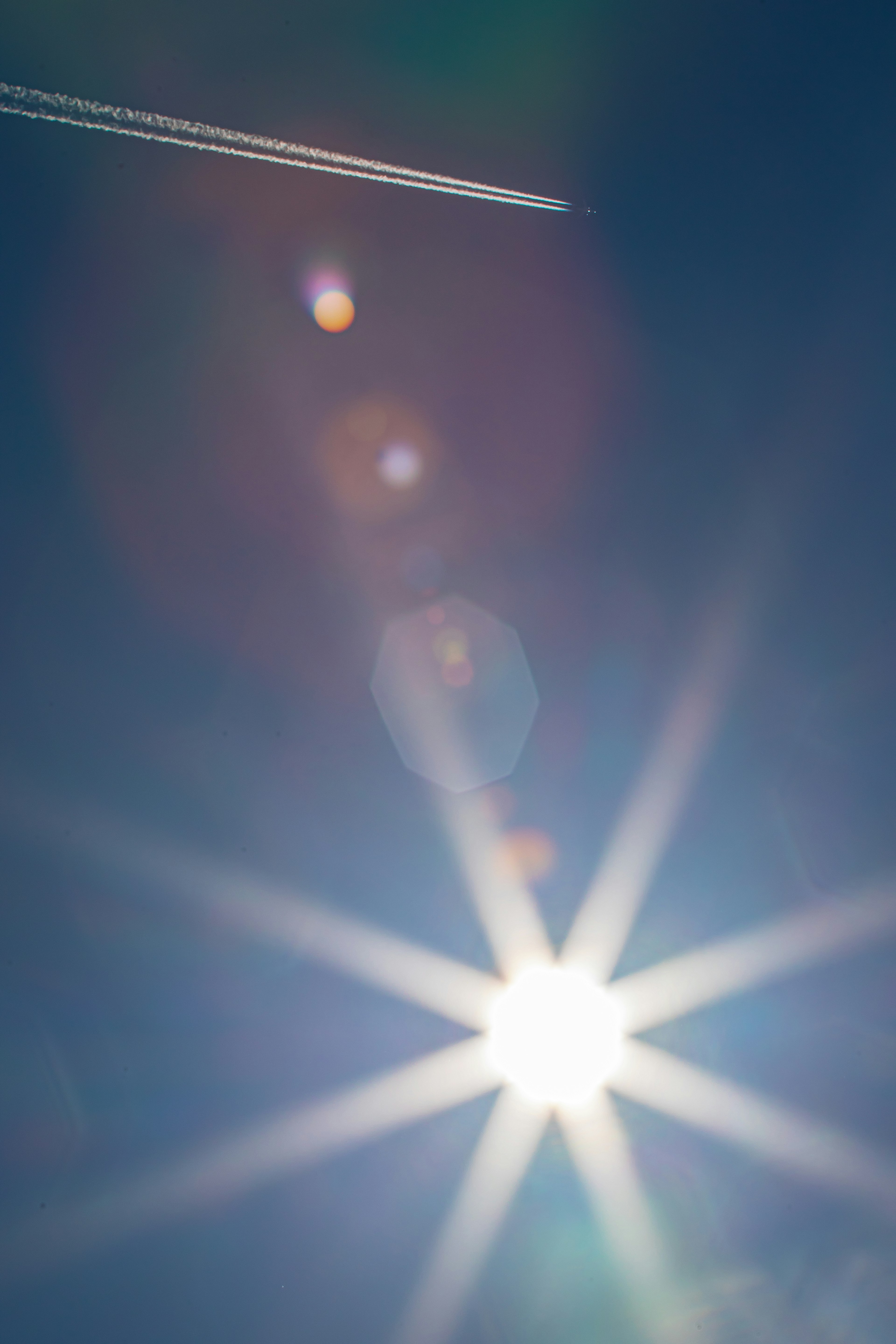 Bright sunlight shining in a clear blue sky with a contrail