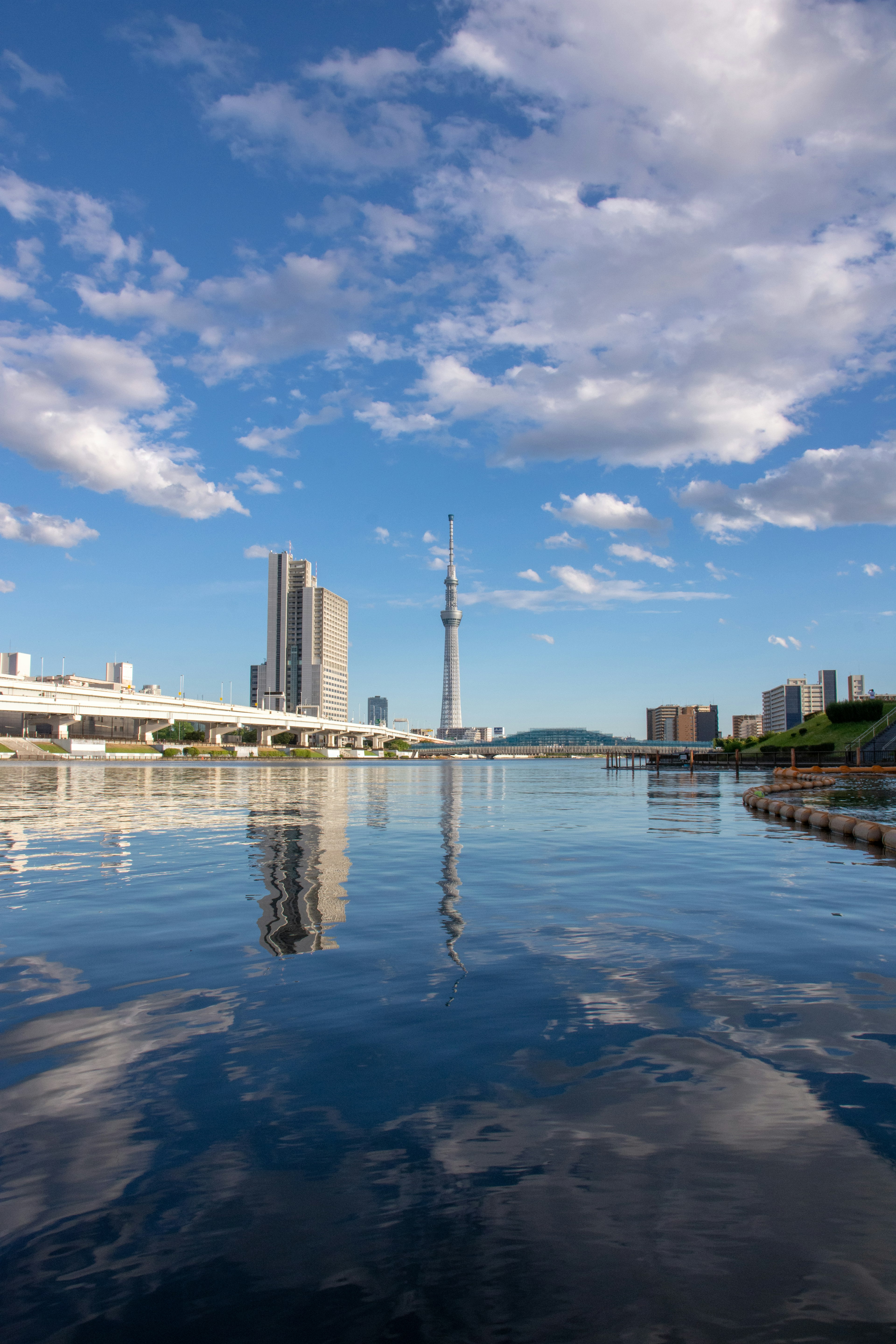 Scenic view of a city skyline with a tower reflecting on calm water under a blue sky