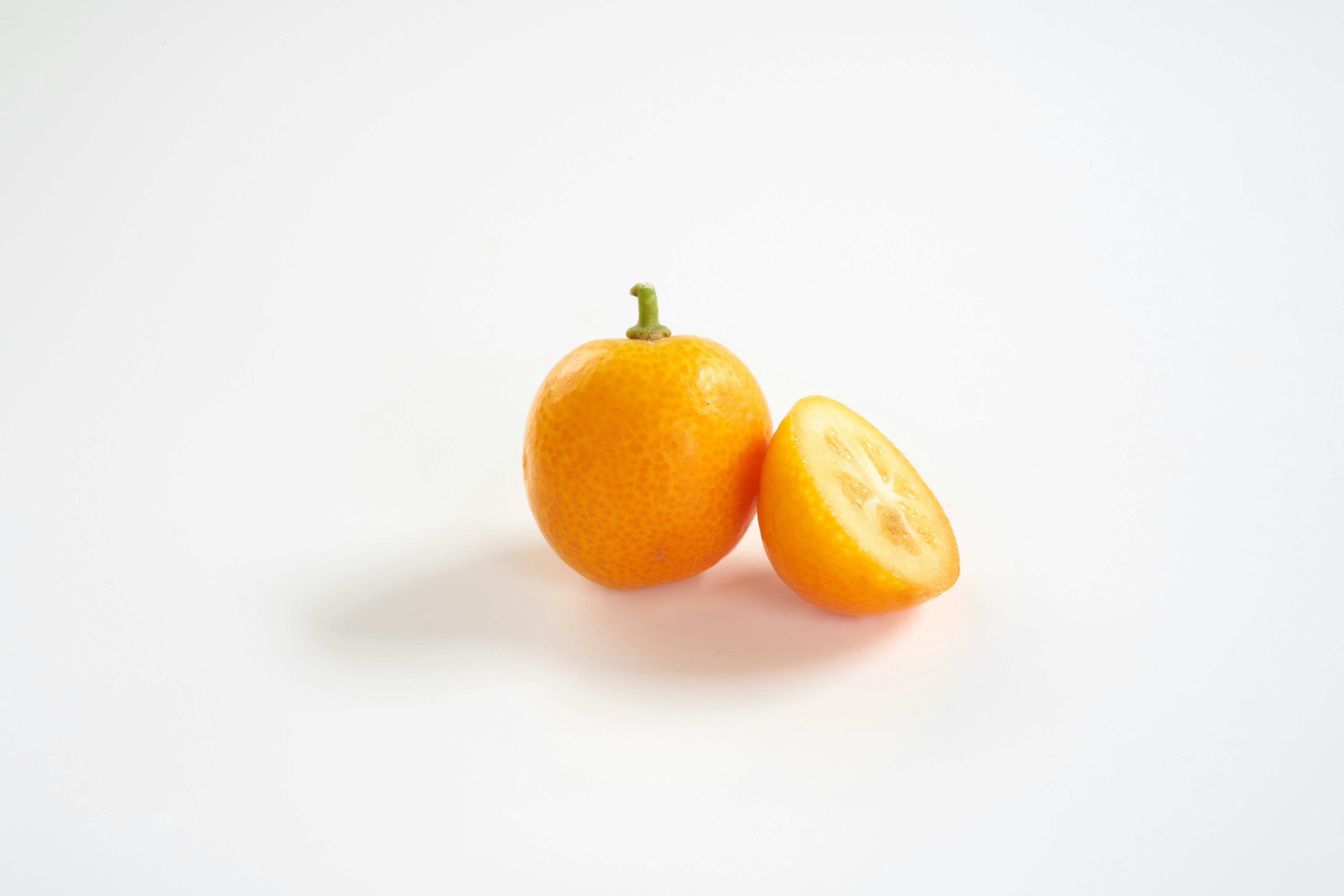 An orange fruit with a sliced half on a white background