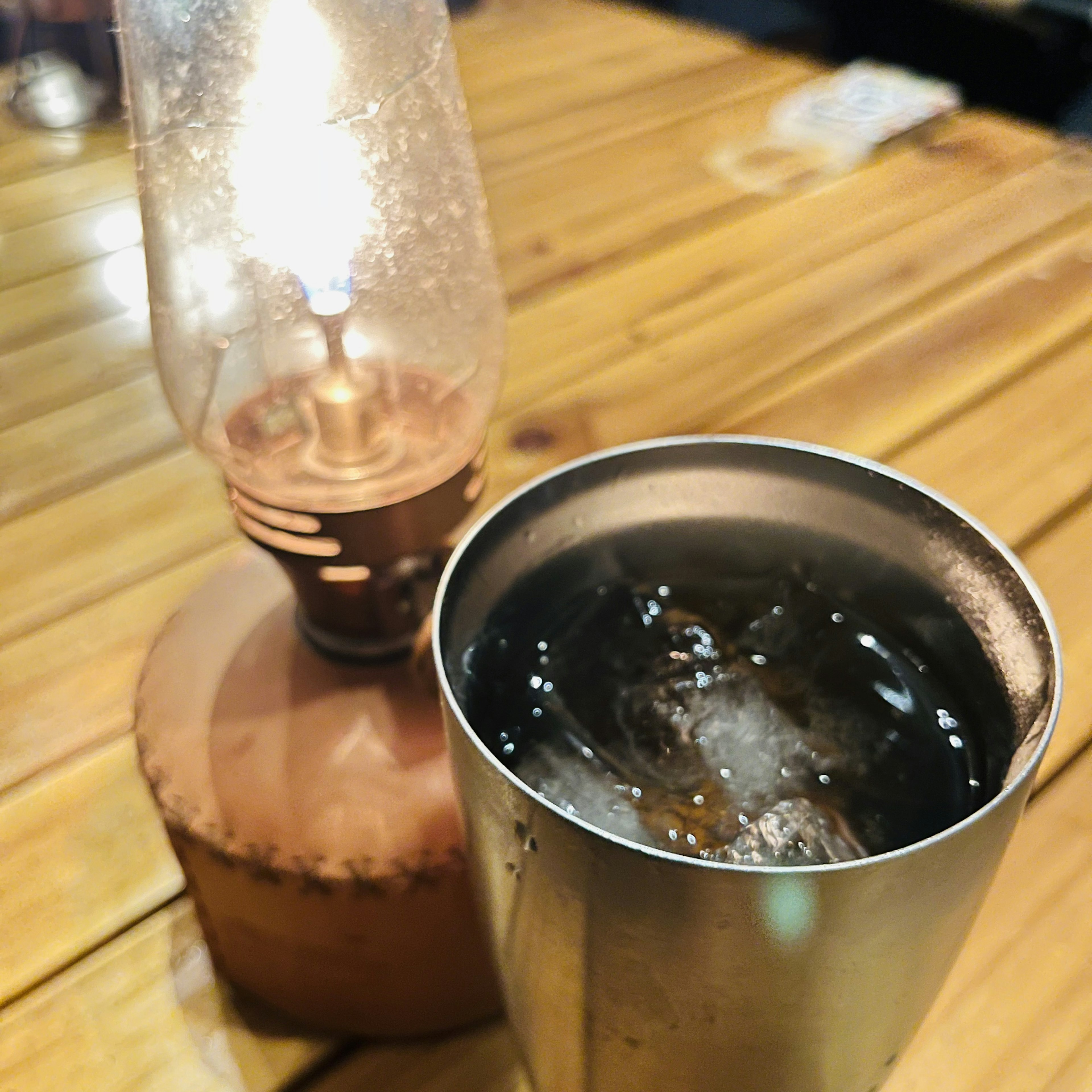 Una lámpara de aceite vintage junto a una taza de metal llena de hielo y bebida