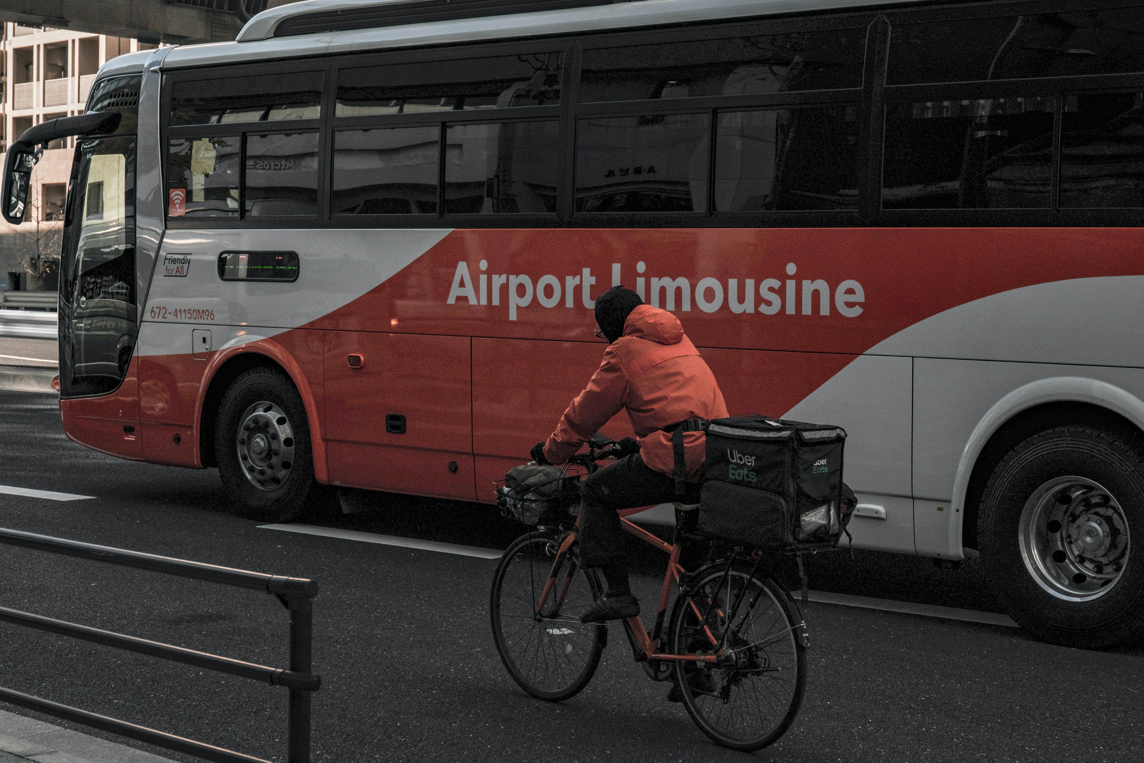 ภาพของรถบัส Airport Limousine ข้างนักปั่นจักรยานในเสื้อแจ็คเก็ตสีส้ม