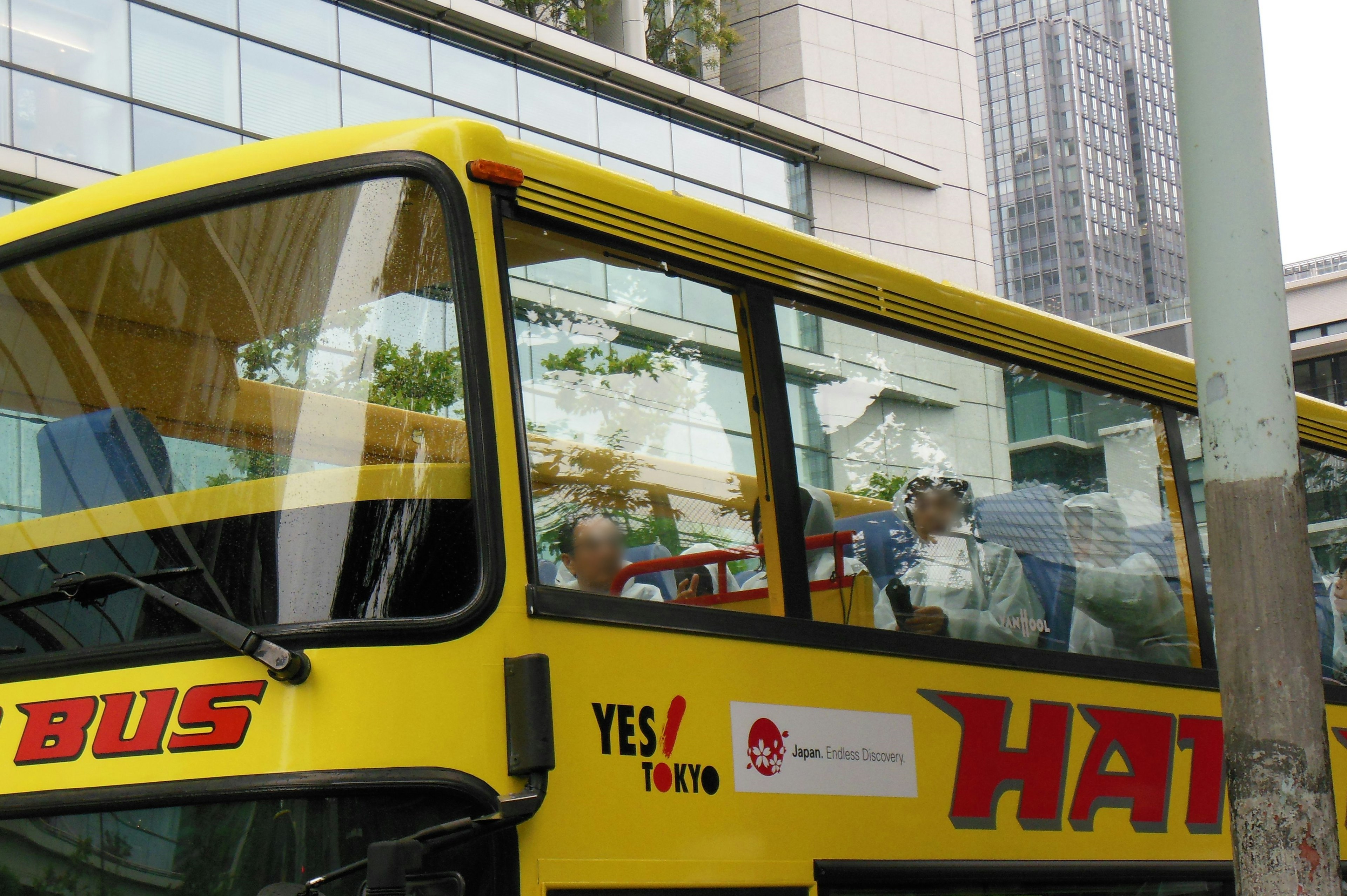 A yellow bus with large letters reading HAT on its side People are visible inside the bus with buildings in the background