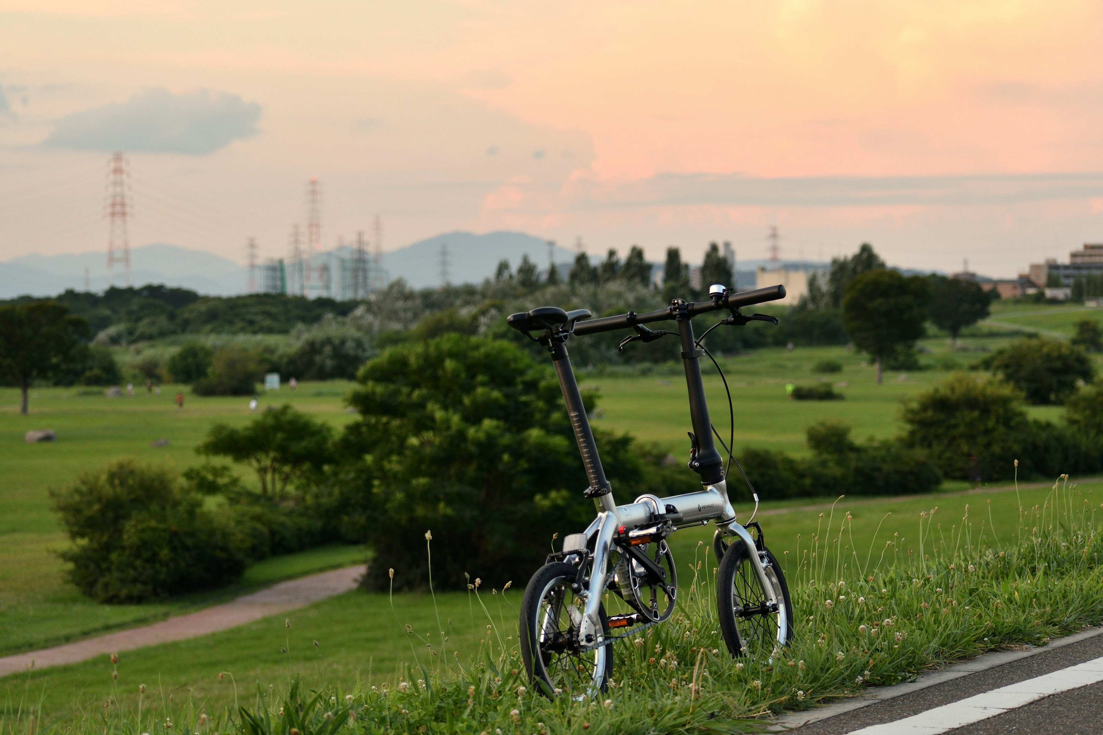 夕焼けの中に立つ折りたたみ自転車と広がる緑の風景