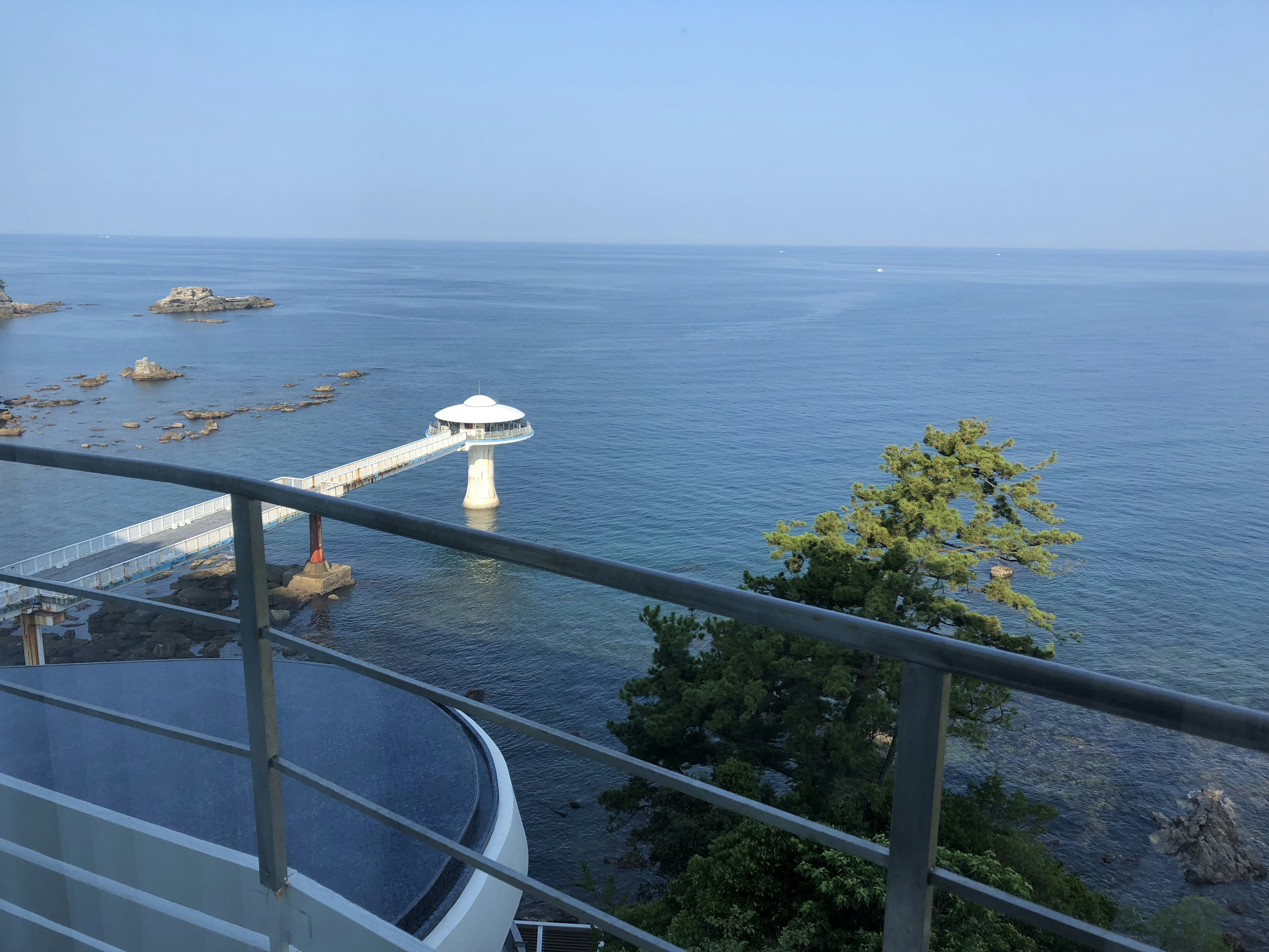 Blick von einem Balkon auf das blaue Meer und den Himmel mit einem Pier