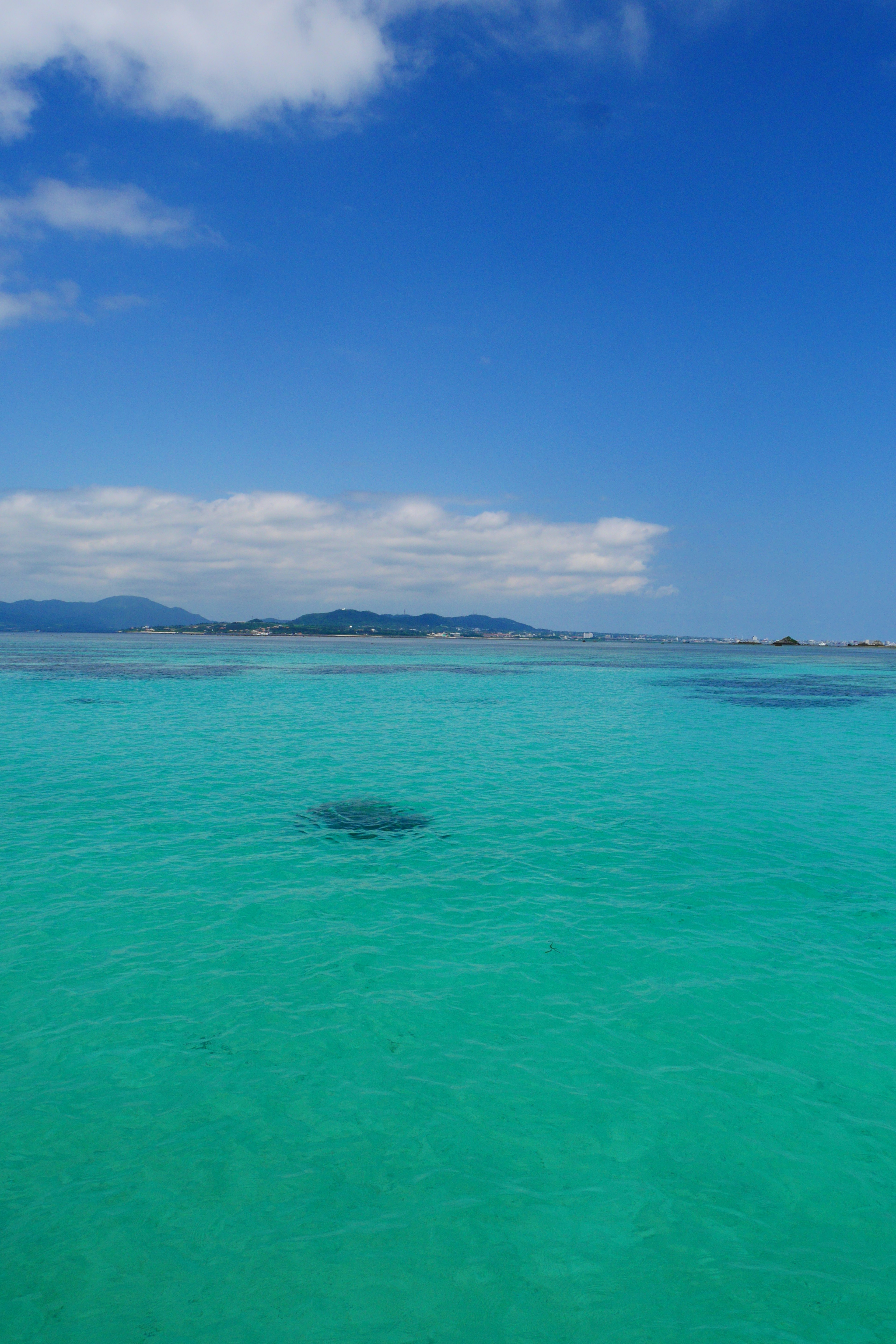 Clear emerald green sea with blue sky and distant islands