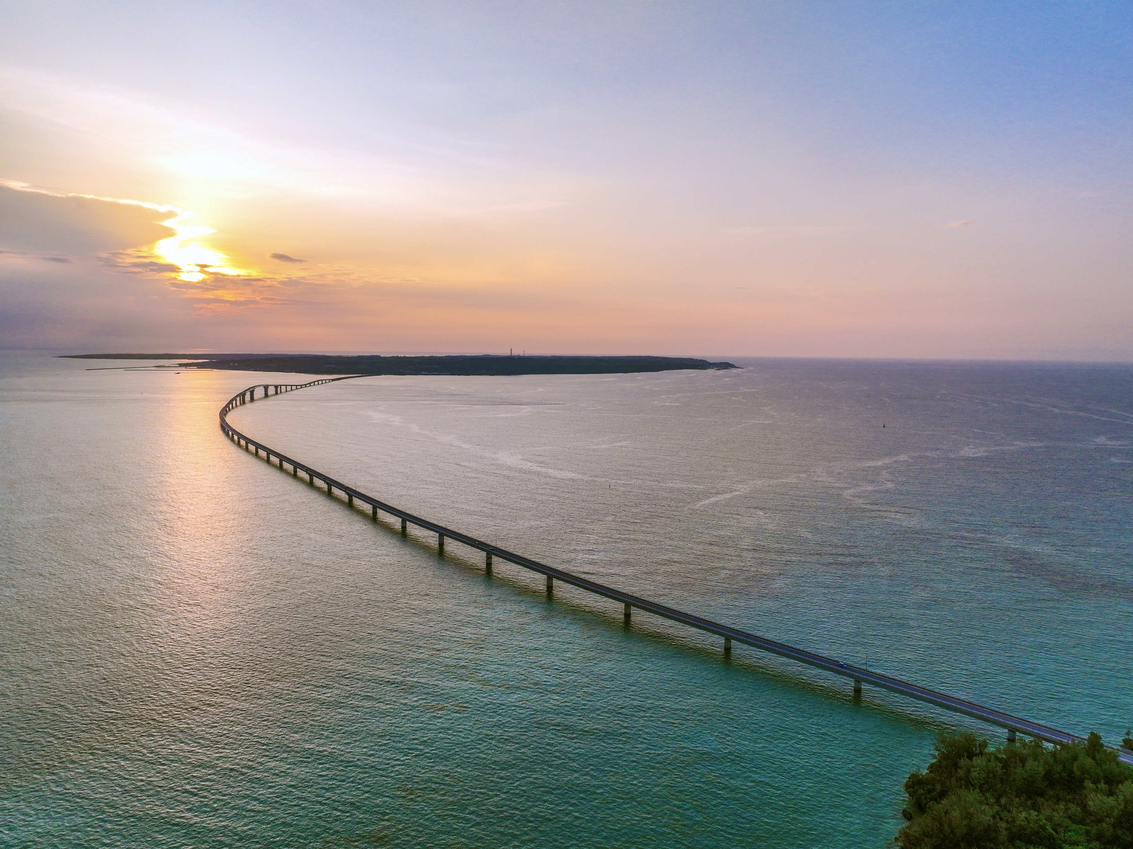 Jembatan panjang di atas air biru dengan matahari terbenam di latar belakang