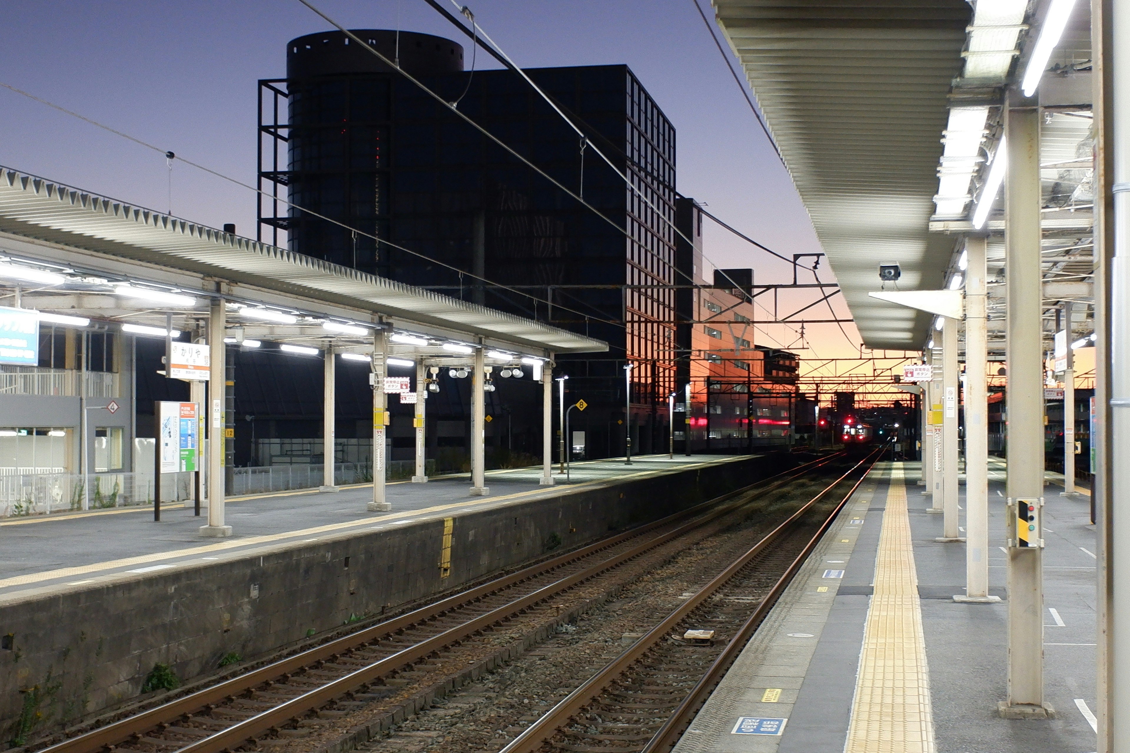 ชานชาลาสถานีรถไฟในยามพลบค่ำที่มีรางและอาคาร