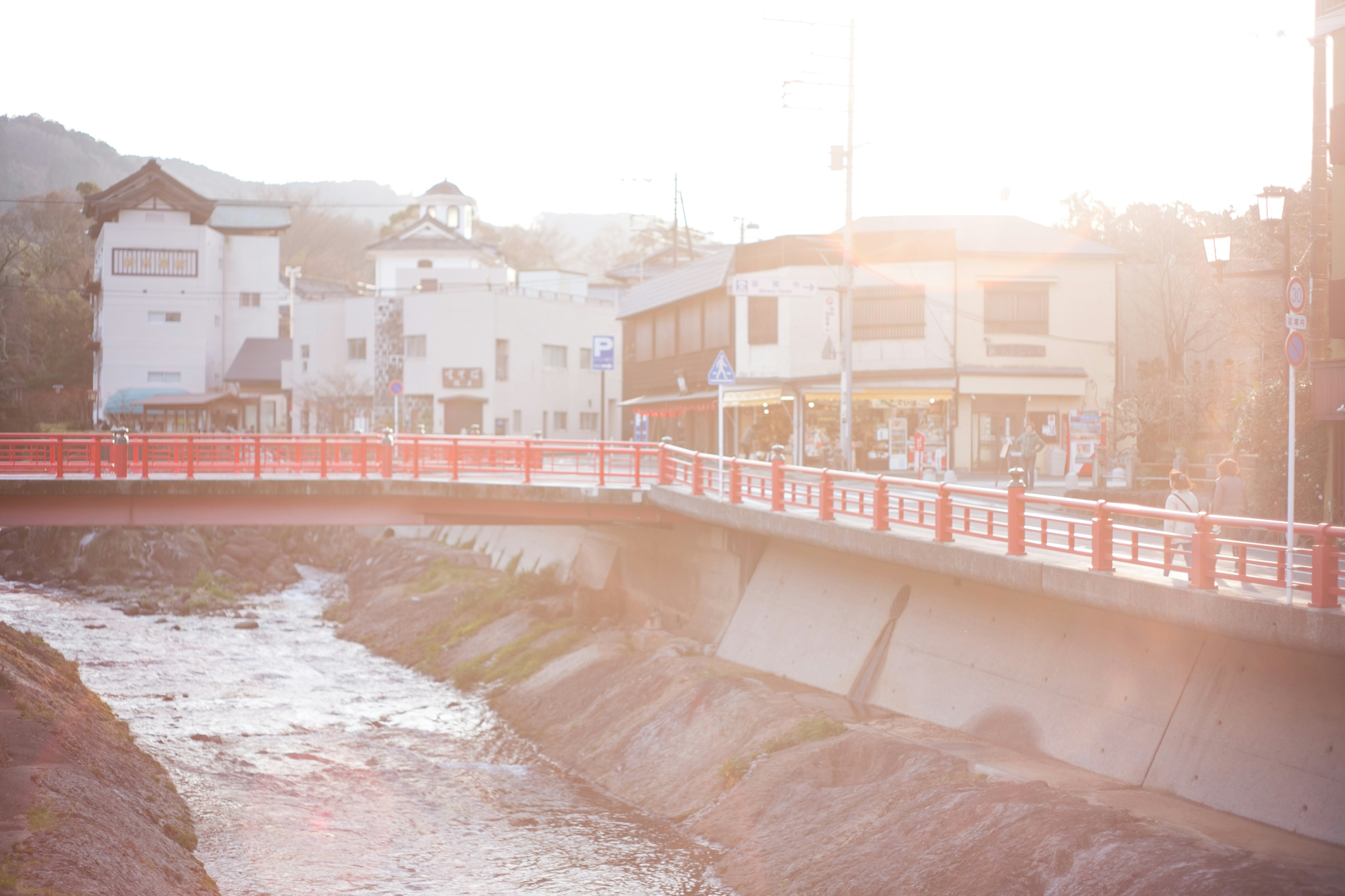 A red bridge over a river with nearby buildings in a soft sunlight