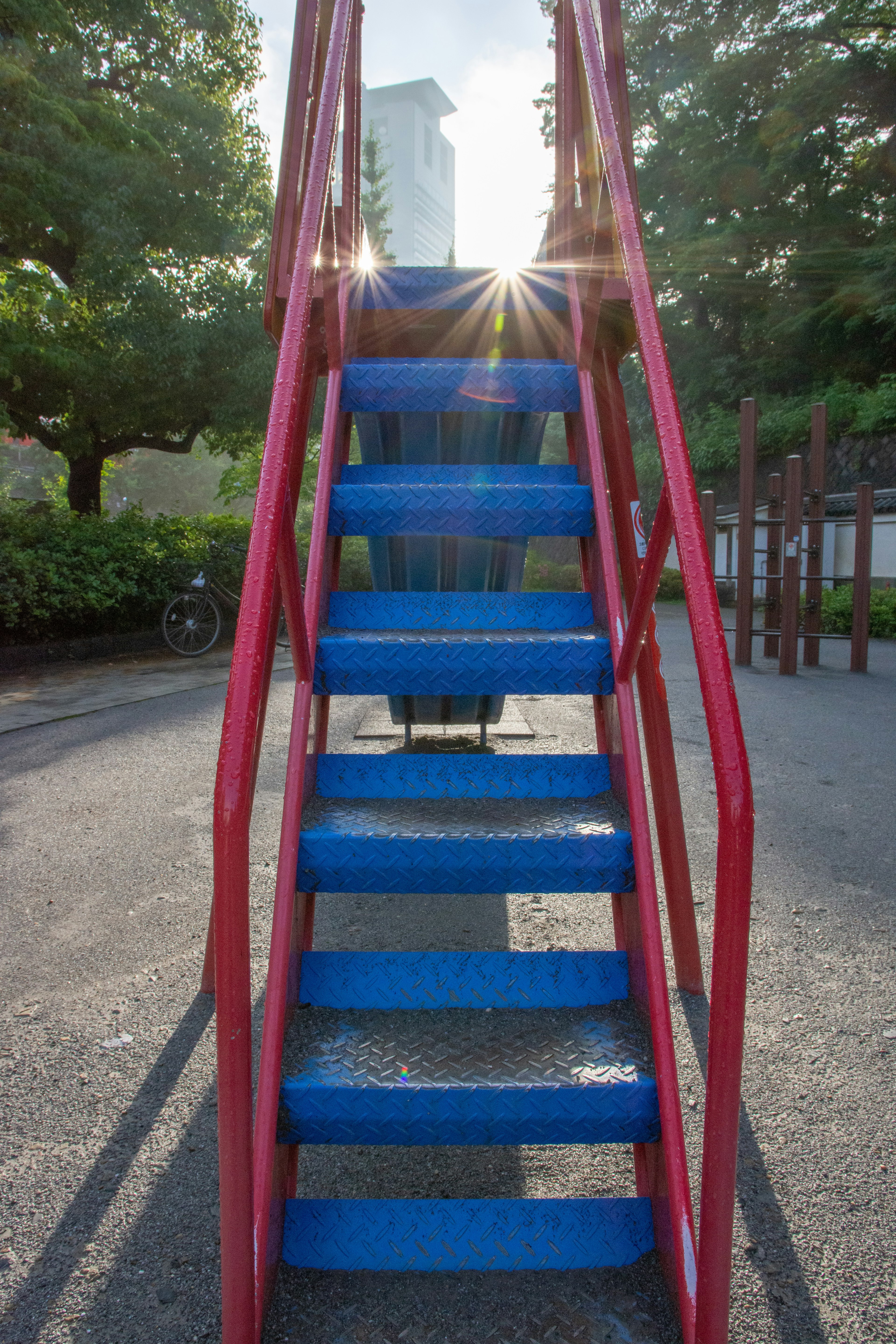 赤い手すりの青い階段が公園にあり太陽の光が差し込んでいる