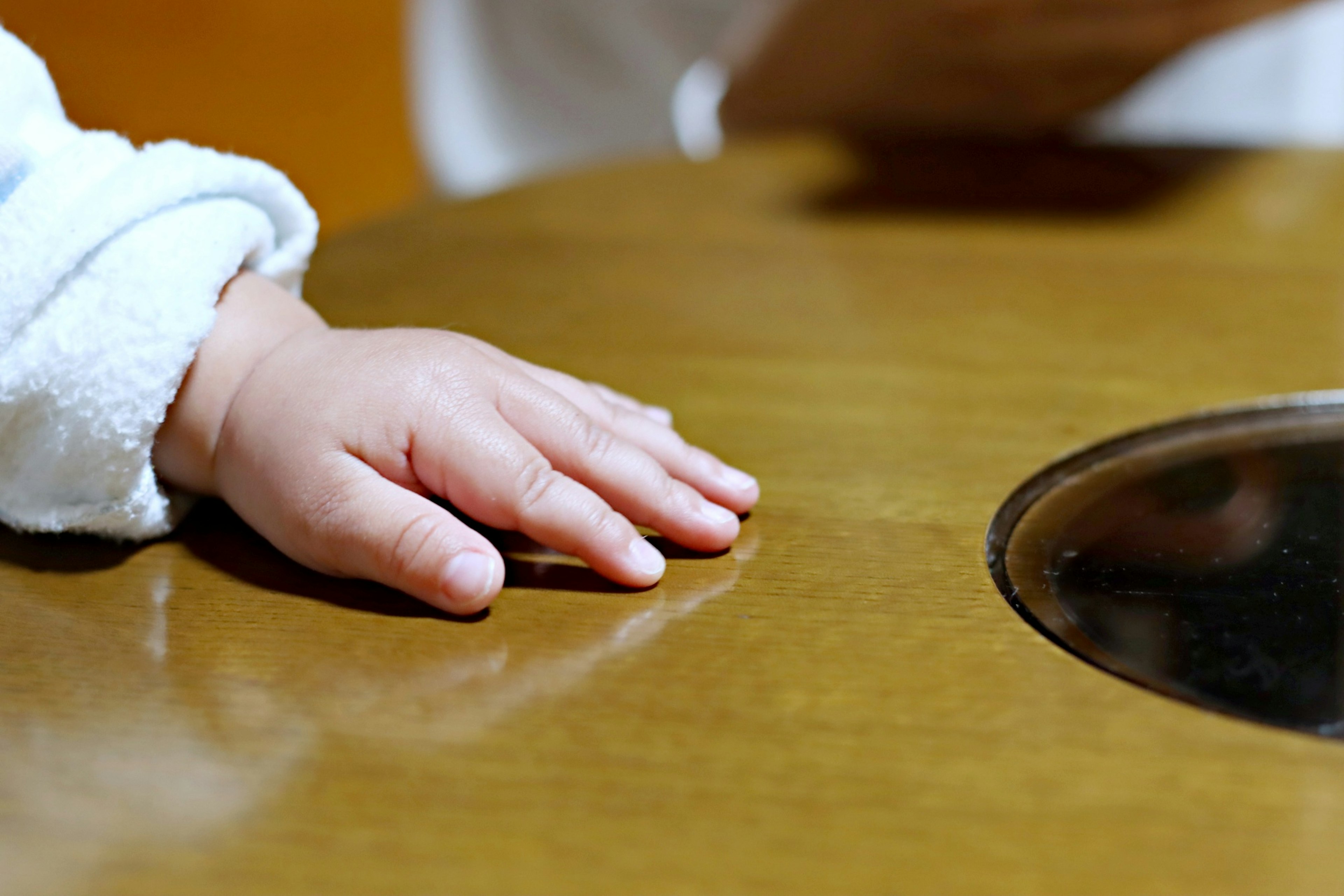 A baby's hand resting on a wooden table with a round cutout