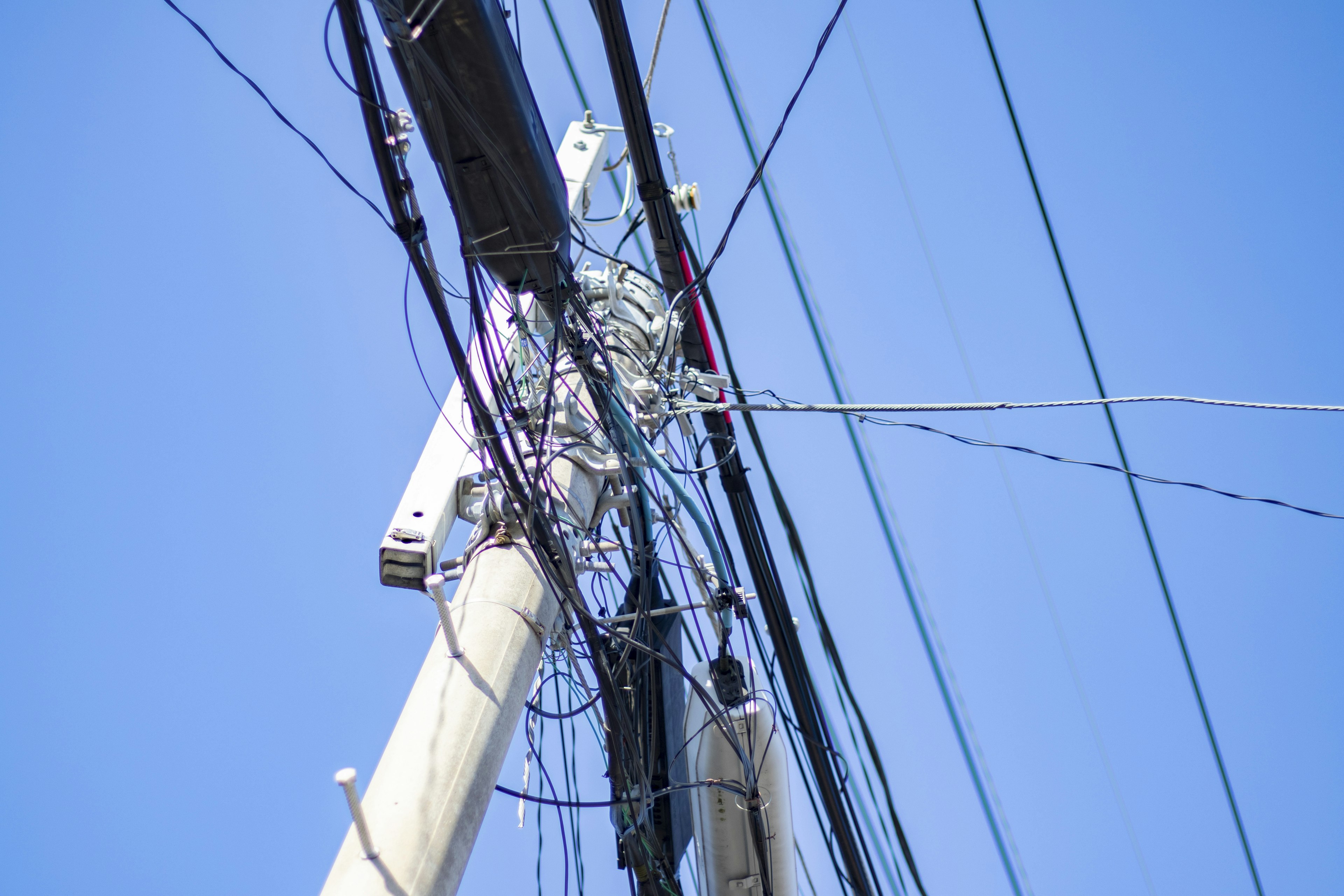 Utility pole with tangled wires against a blue sky