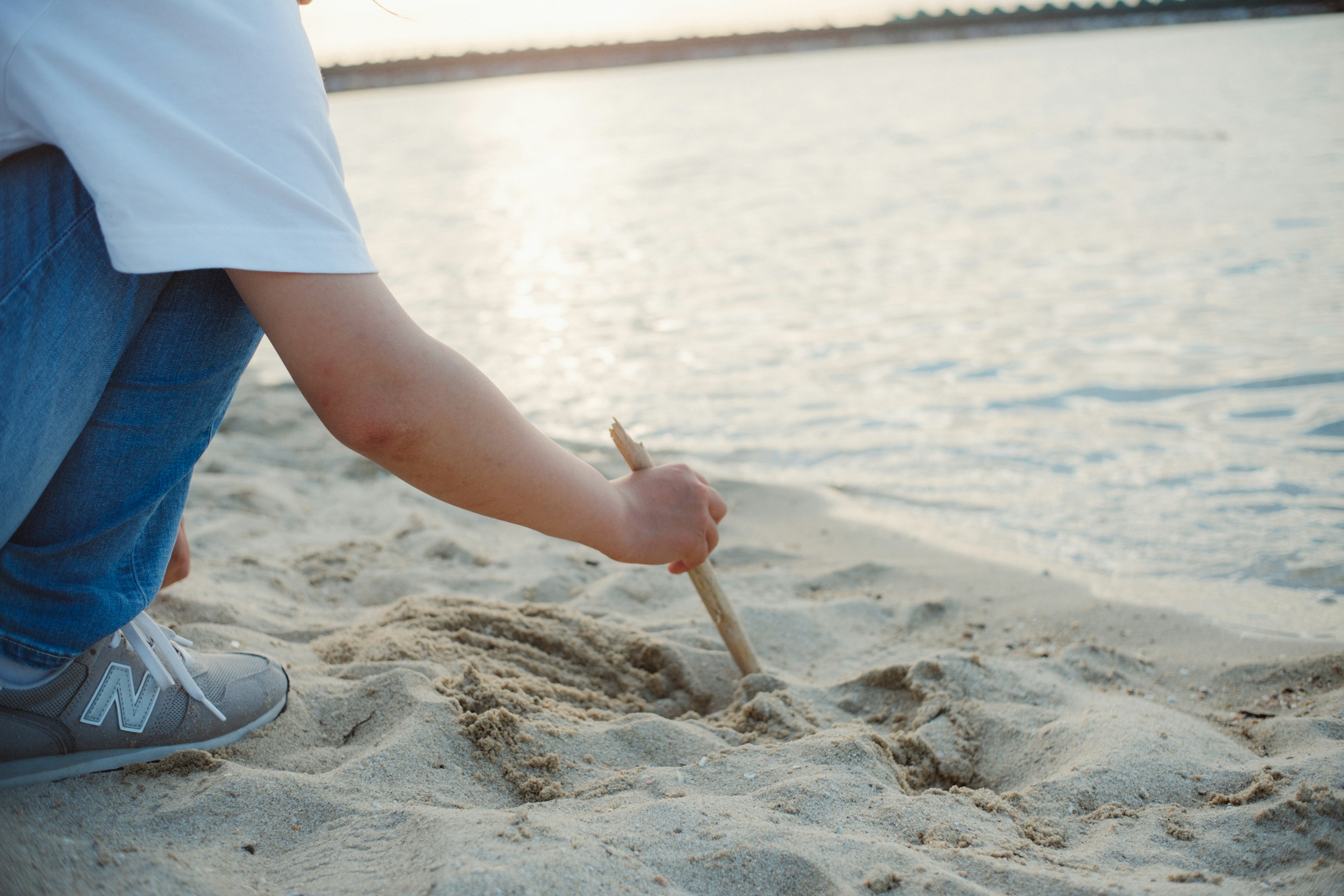 Person, die mit einem Stock im Sand am Strand zeichnet