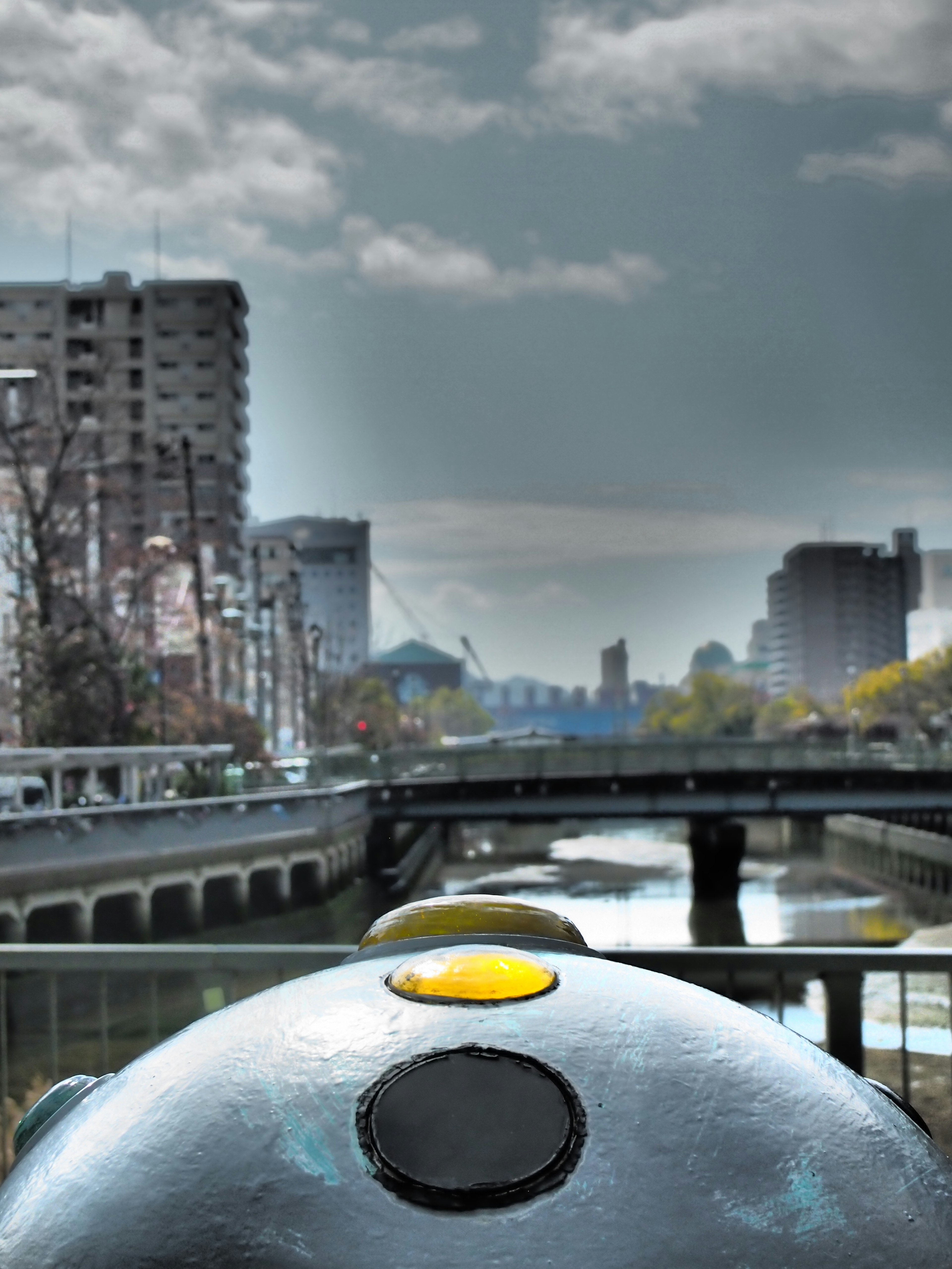 Acercamiento de un objeto redondo con un punto amarillo contra un fondo de río y paisaje urbano