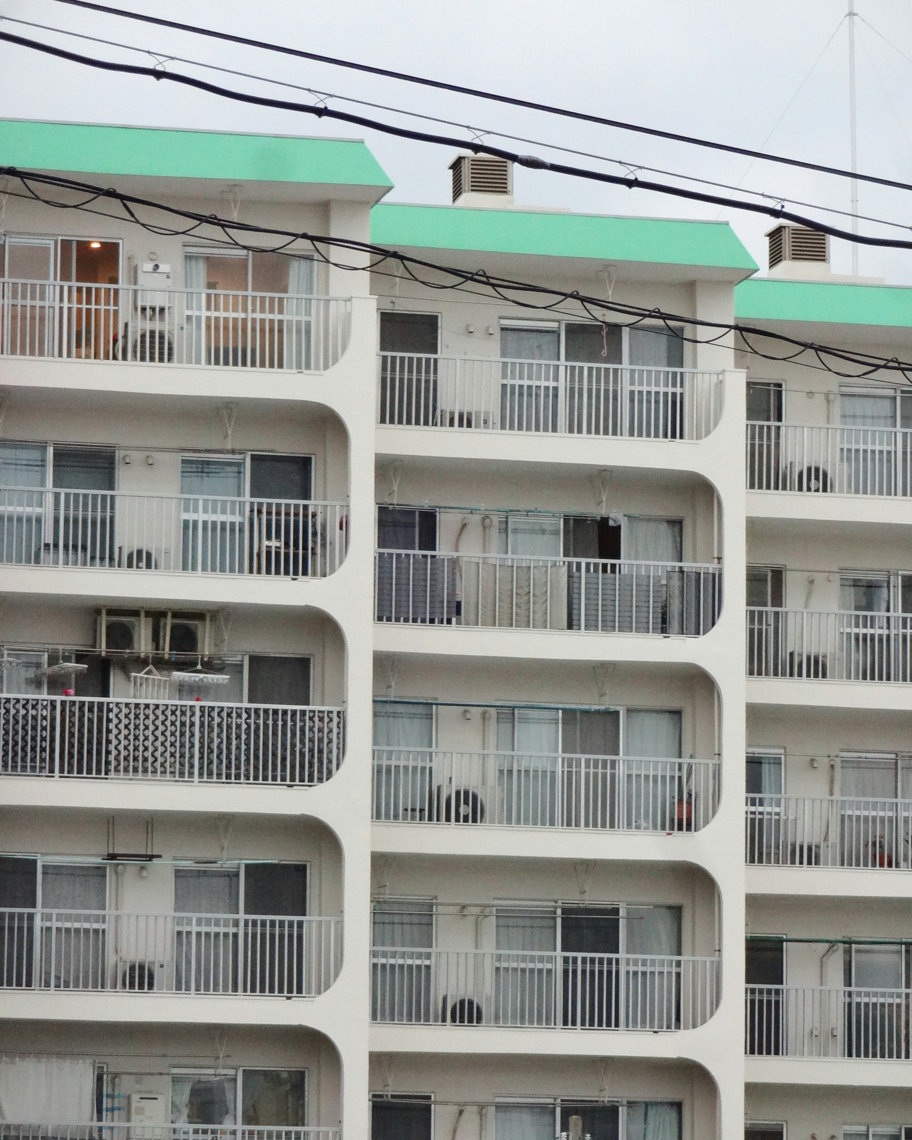 Exterior de un edificio de apartamentos con techo verde balcones en cada piso unidades de aire acondicionado visibles