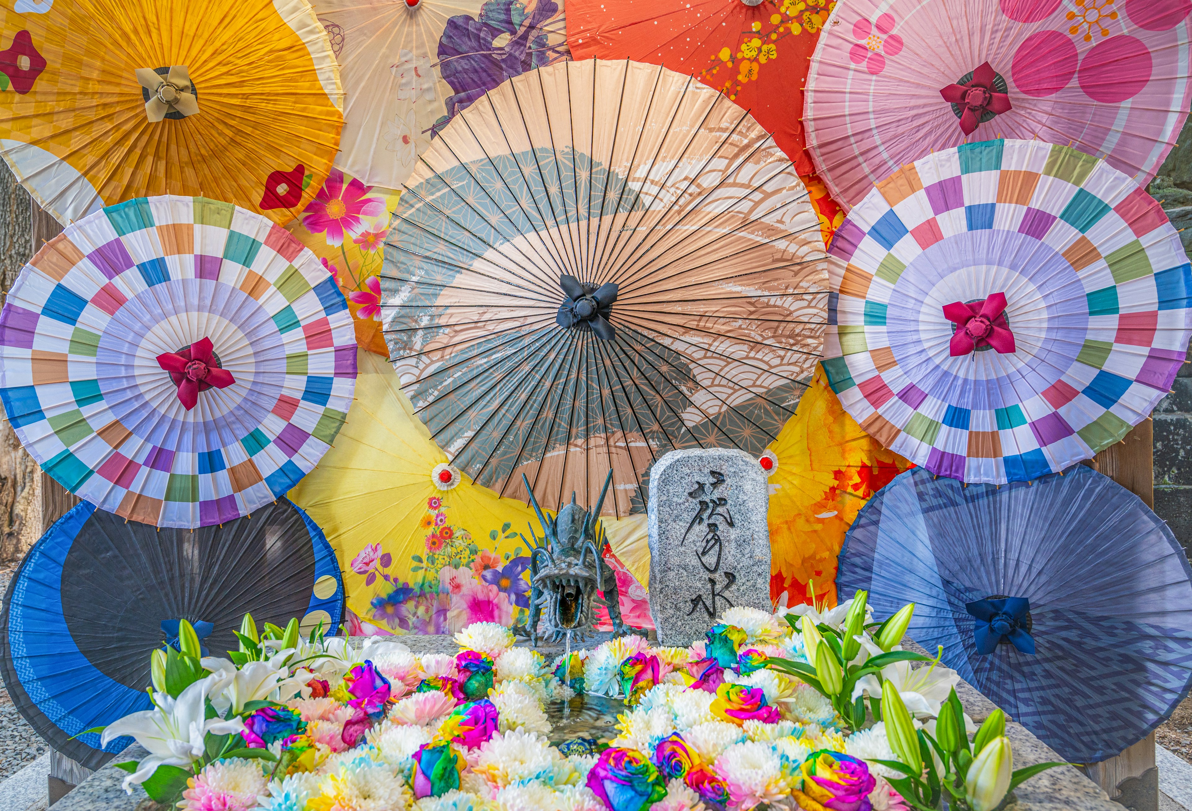 Colorful Japanese umbrellas arranged behind a floral decoration featuring a statue