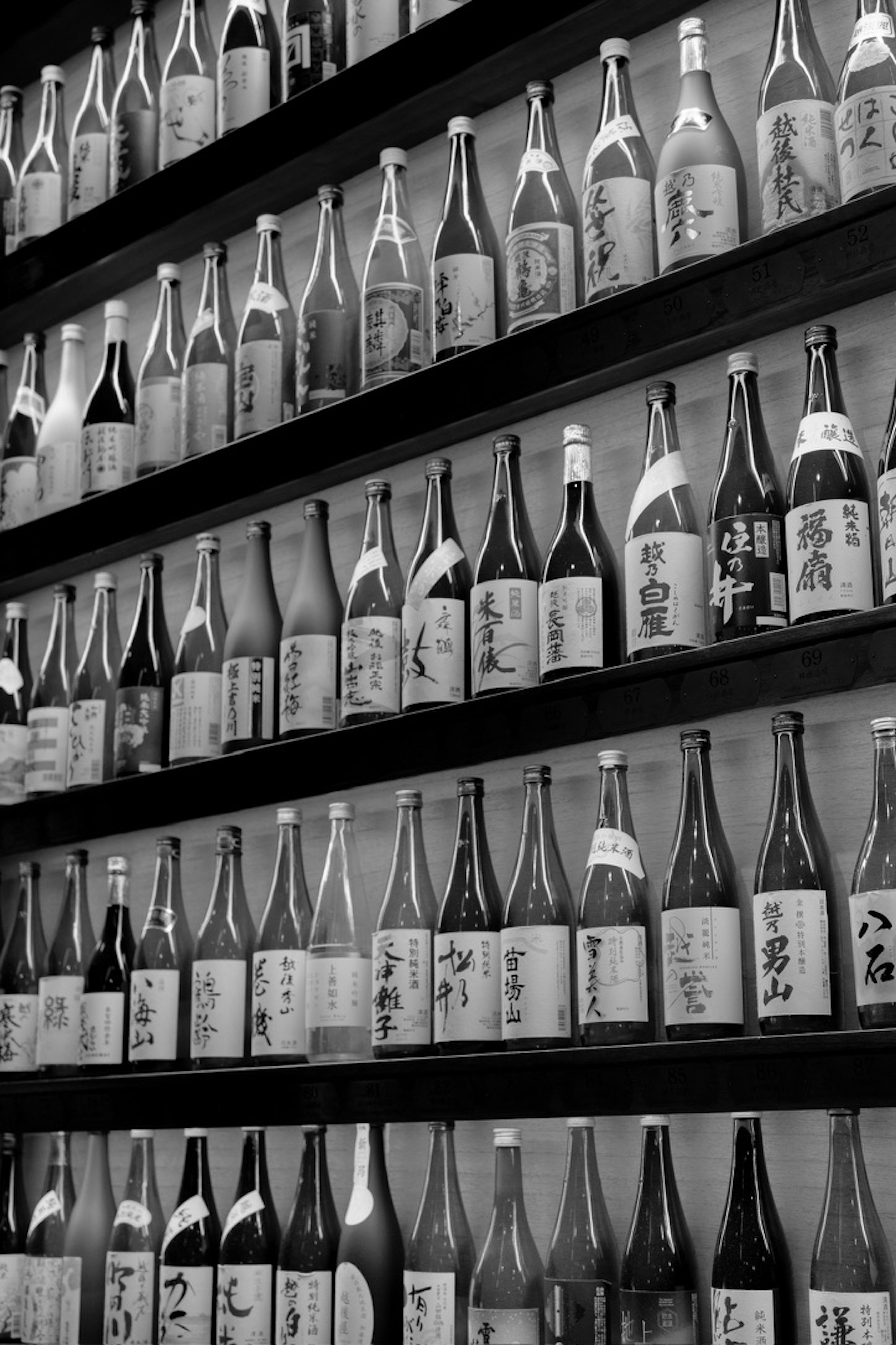 Exhibición de botellas de sake en blanco y negro dispuestas en una pared