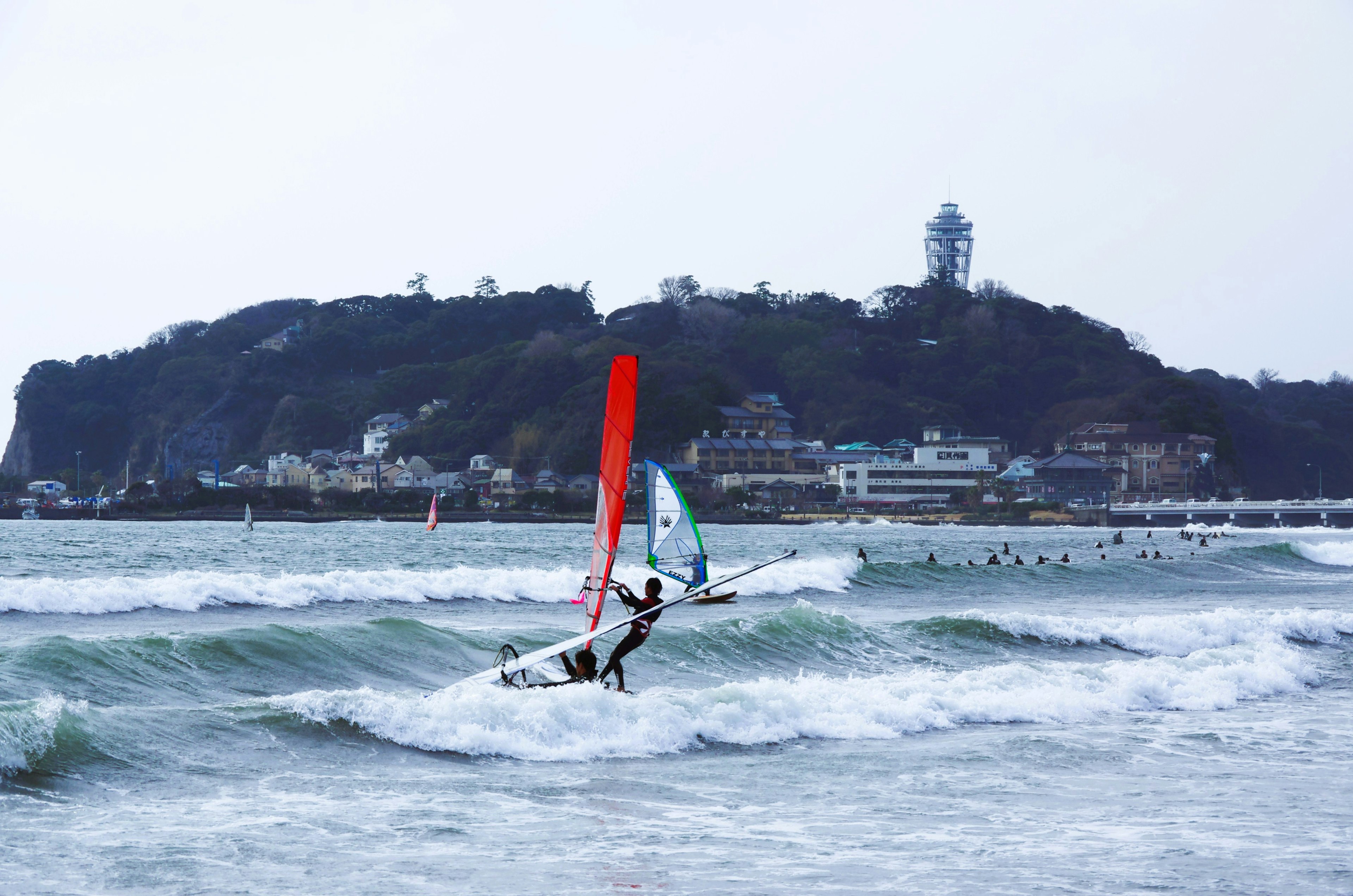 海でウィンドサーフィンを楽しむ人と背景に灯台のある風景