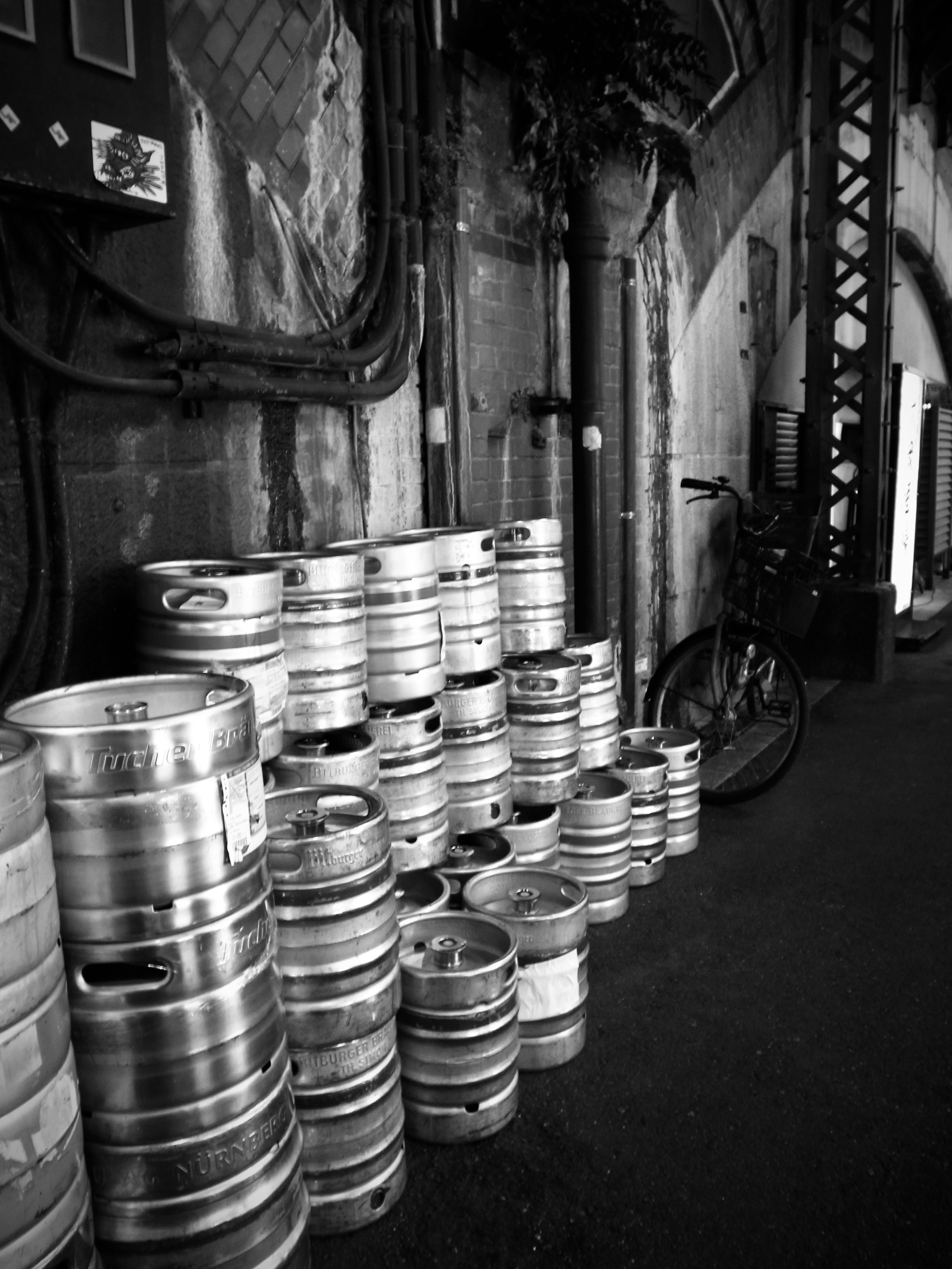 Stack of beer kegs against a textured wall with a bicycle nearby