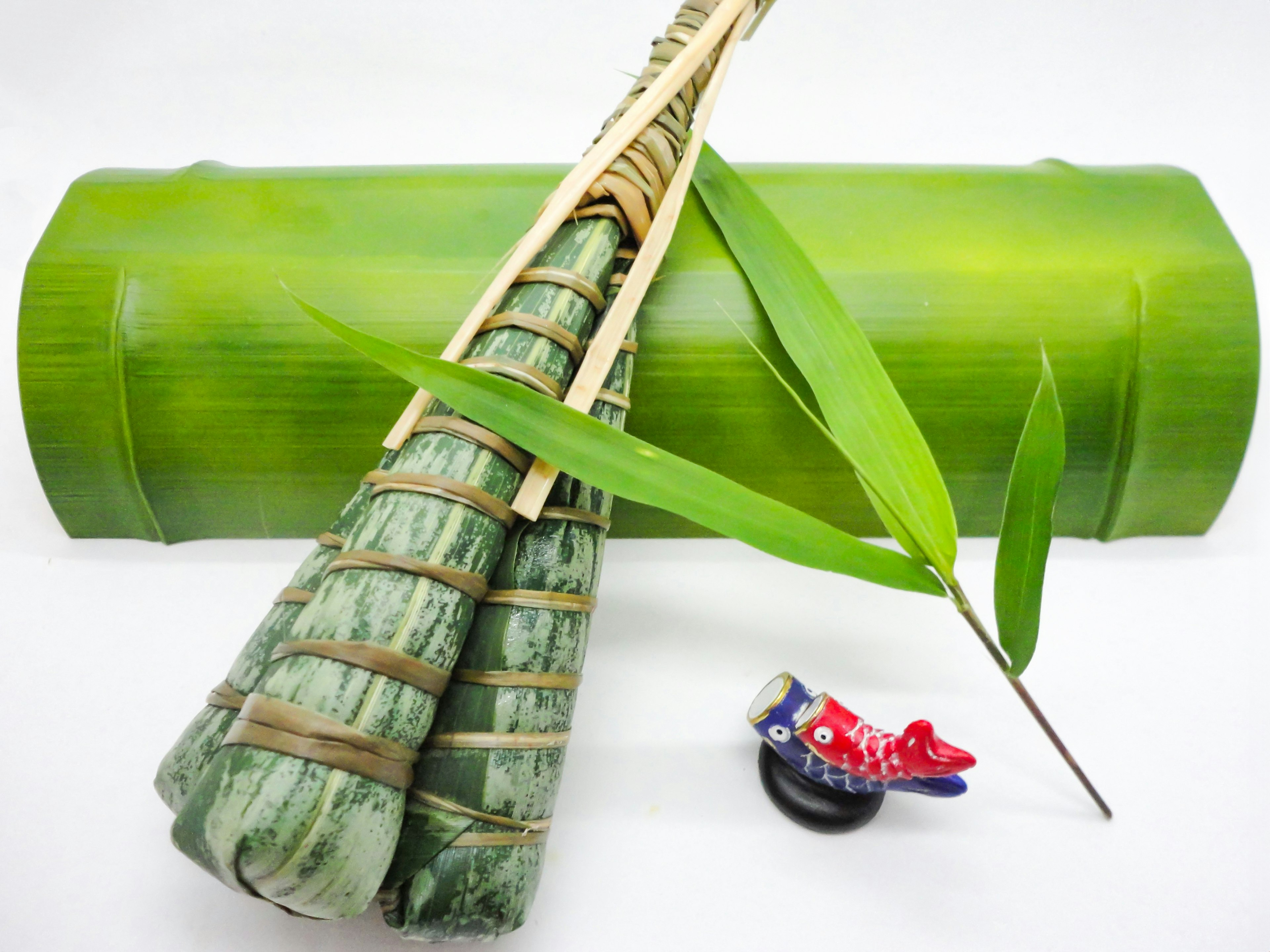 Wrapped food made with leaves placed on green bamboo with a thin leaf beside it