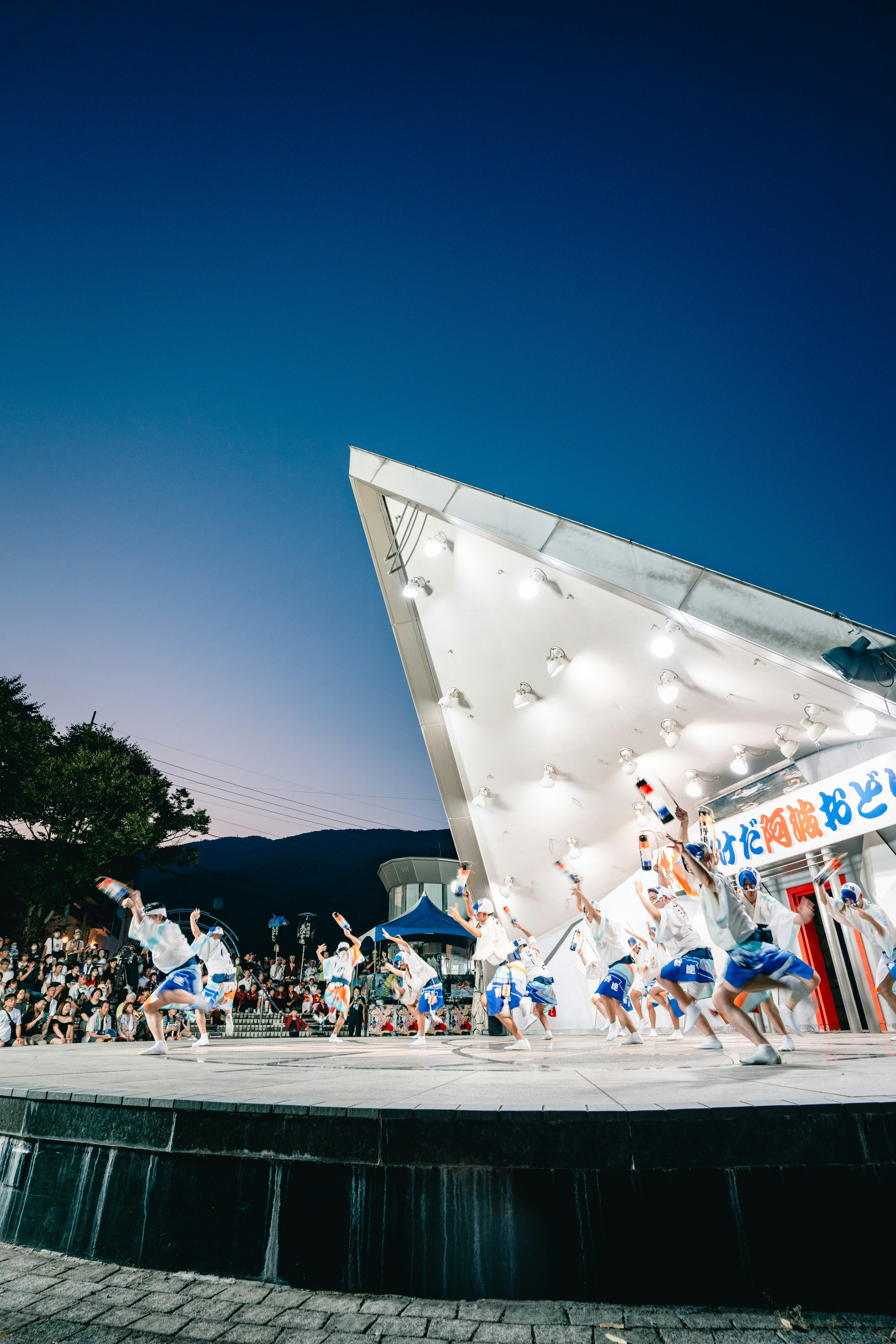 青い空の下で踊る人々と現代的な建築の舞台