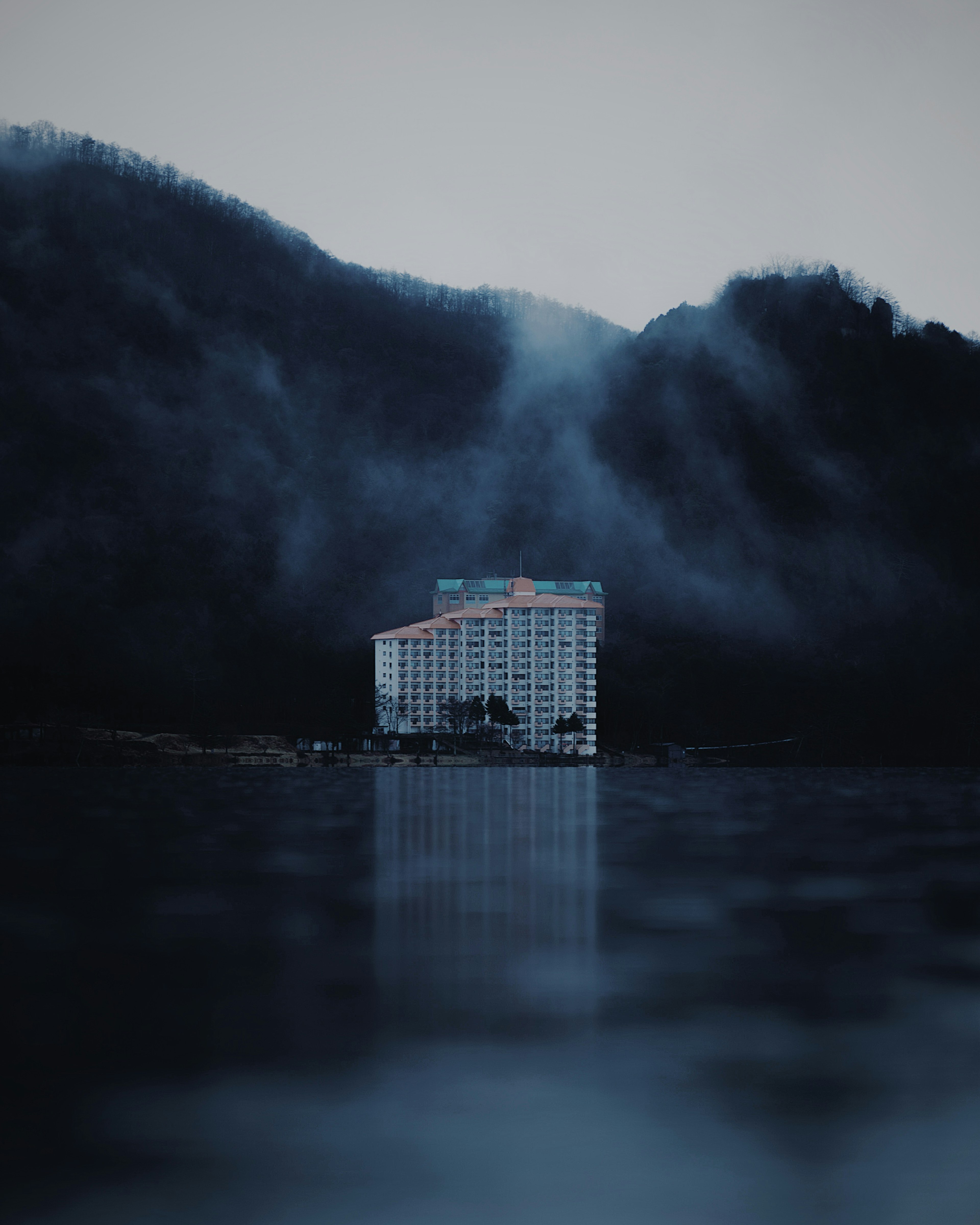 A serene view of a high-rise hotel surrounded by misty mountains