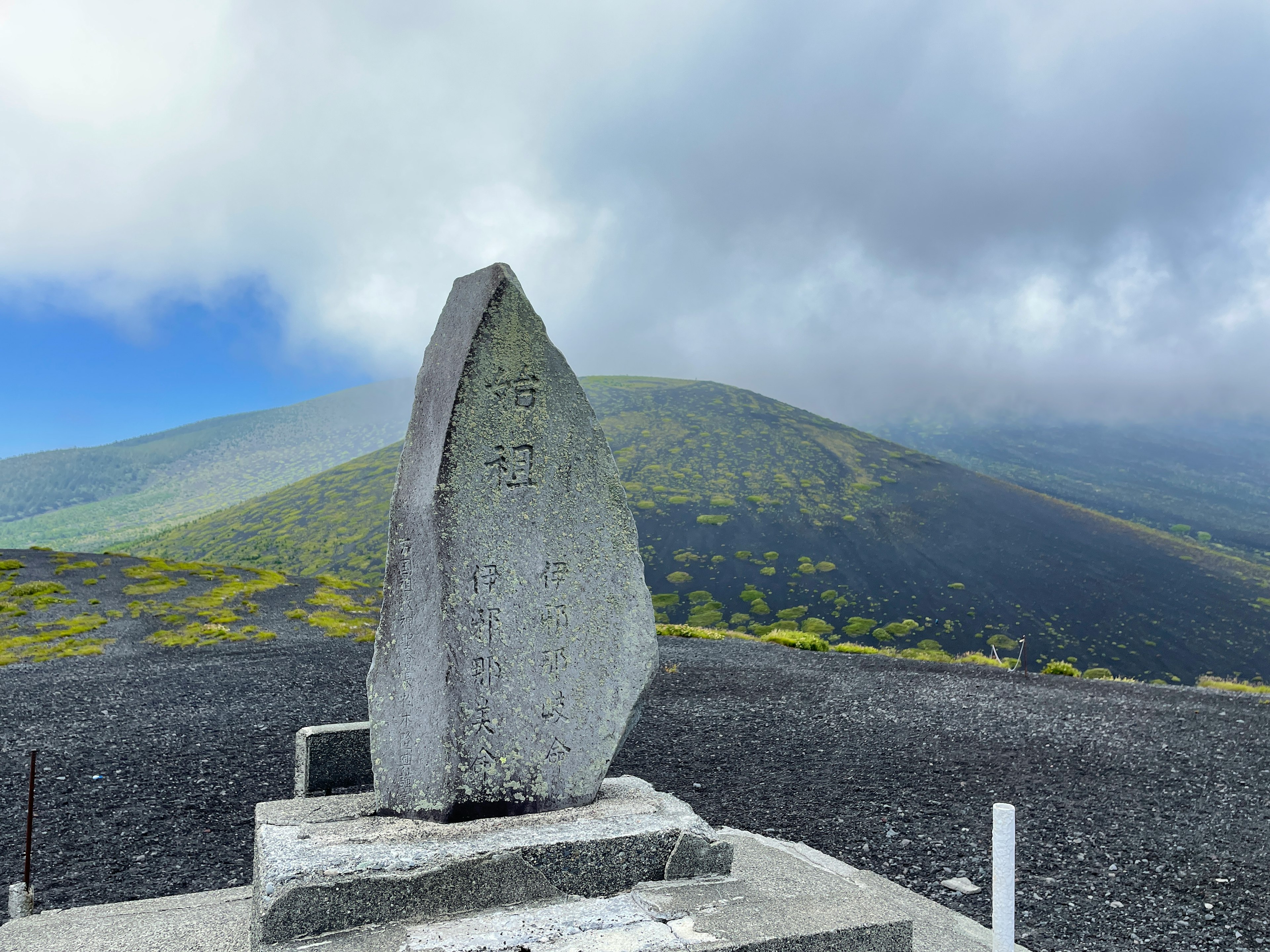 Monumen batu besar di puncak gunung dengan bukit hijau di latar belakang