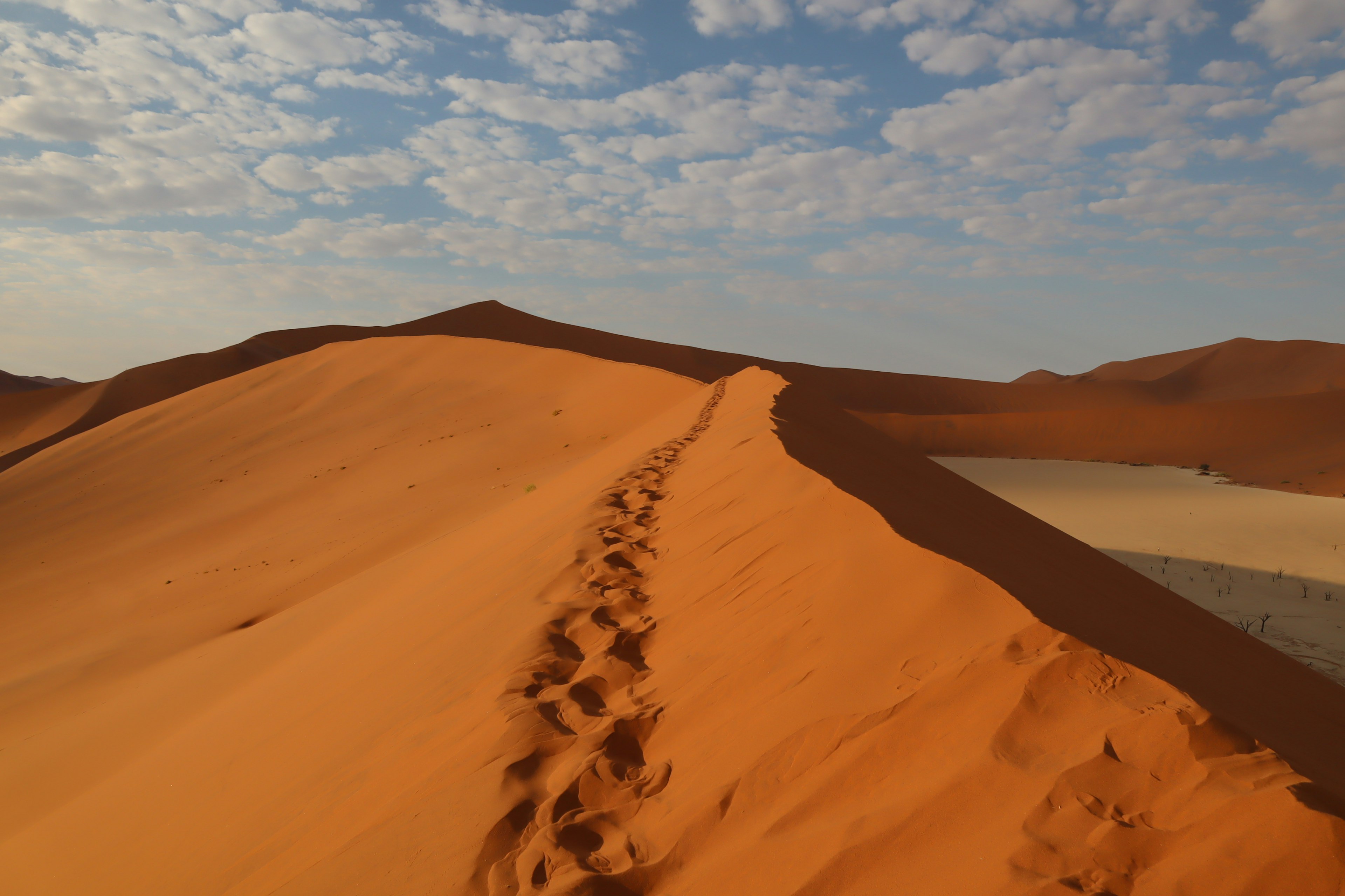 Dune di sabbia arancione che si estendono sotto un cielo blu con nuvole