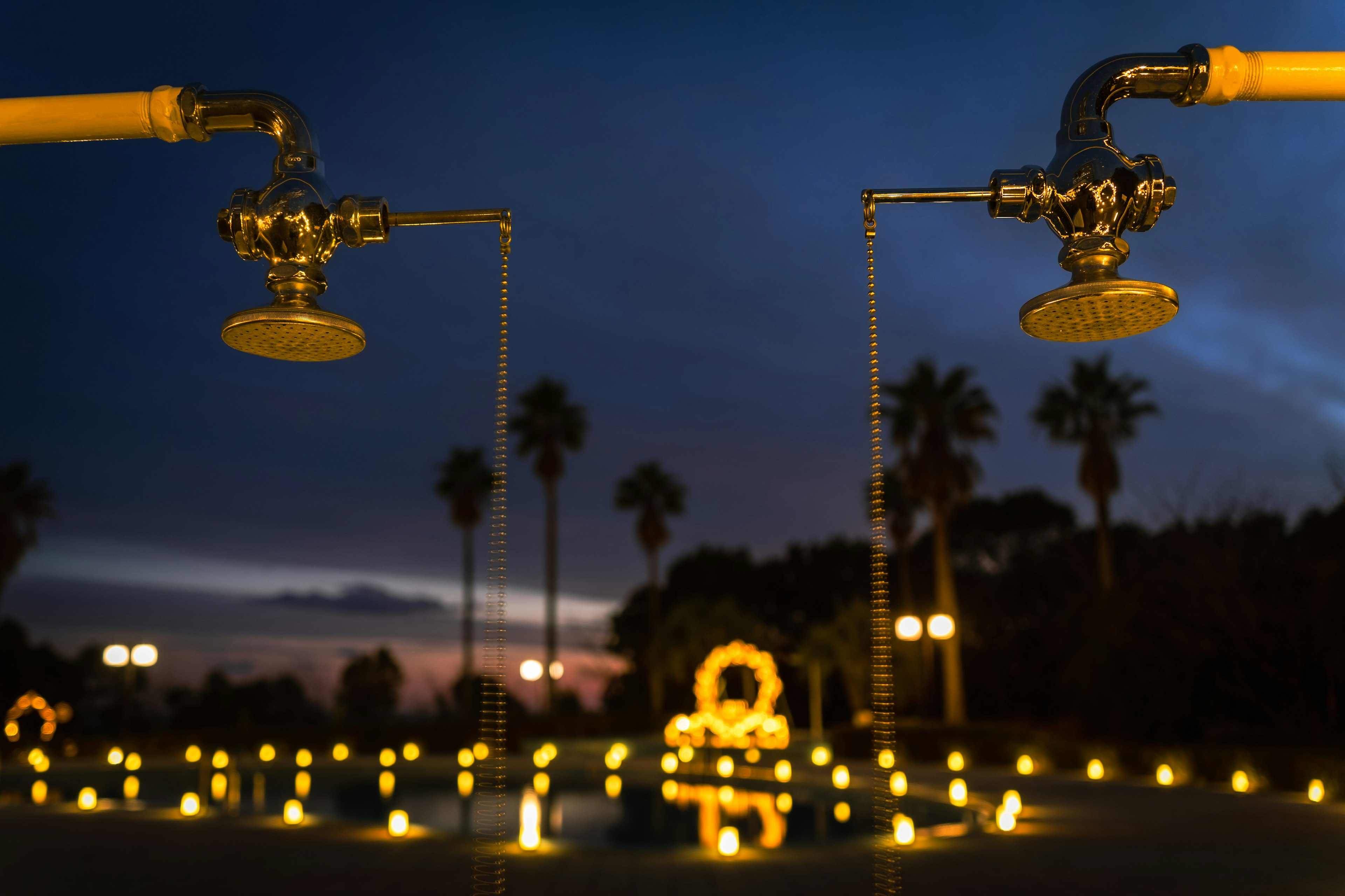 Two shower heads in a garden at dusk surrounded by candles