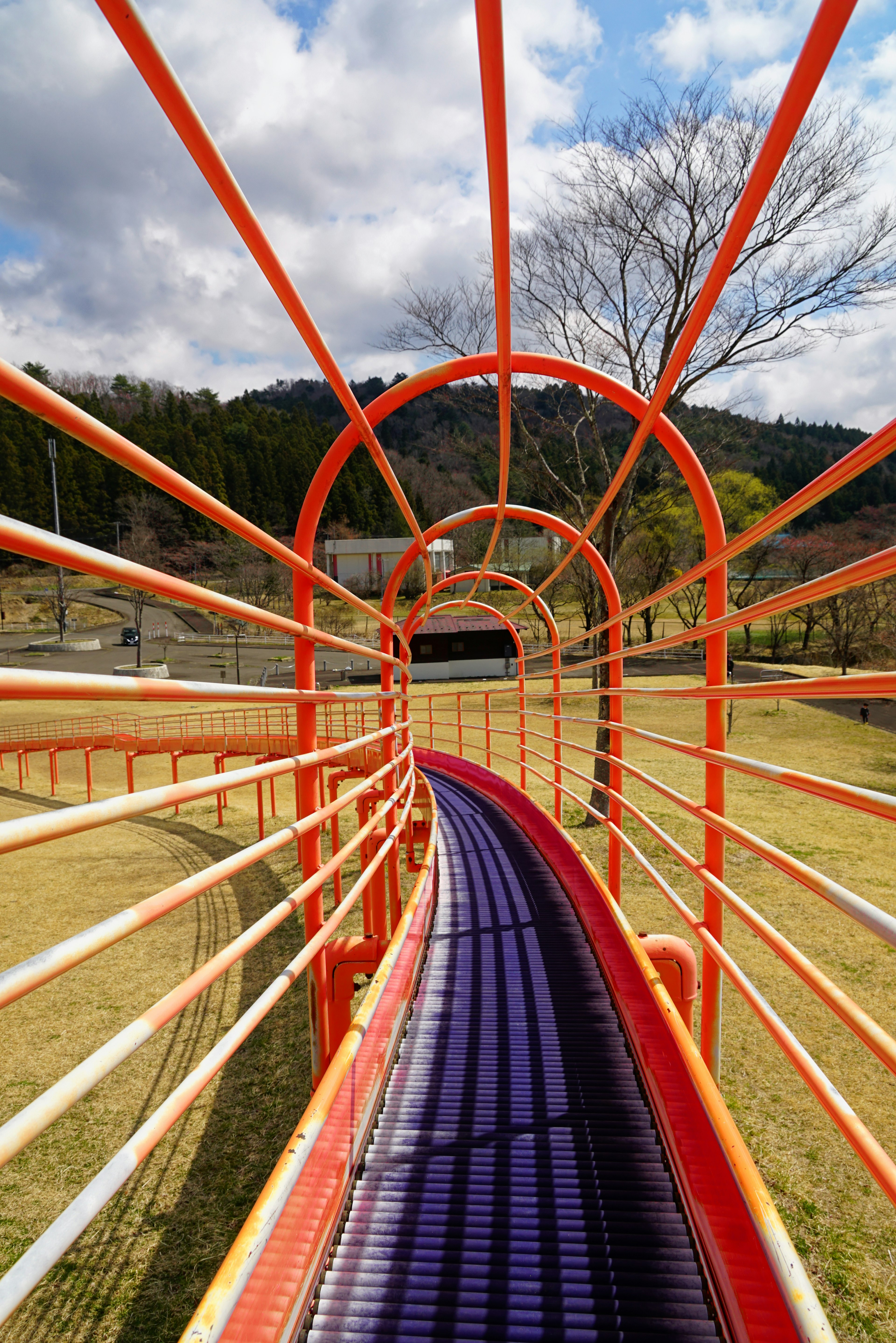 Túnel de juego colorido con tobogán púrpura y marco naranja rodeado de paisaje