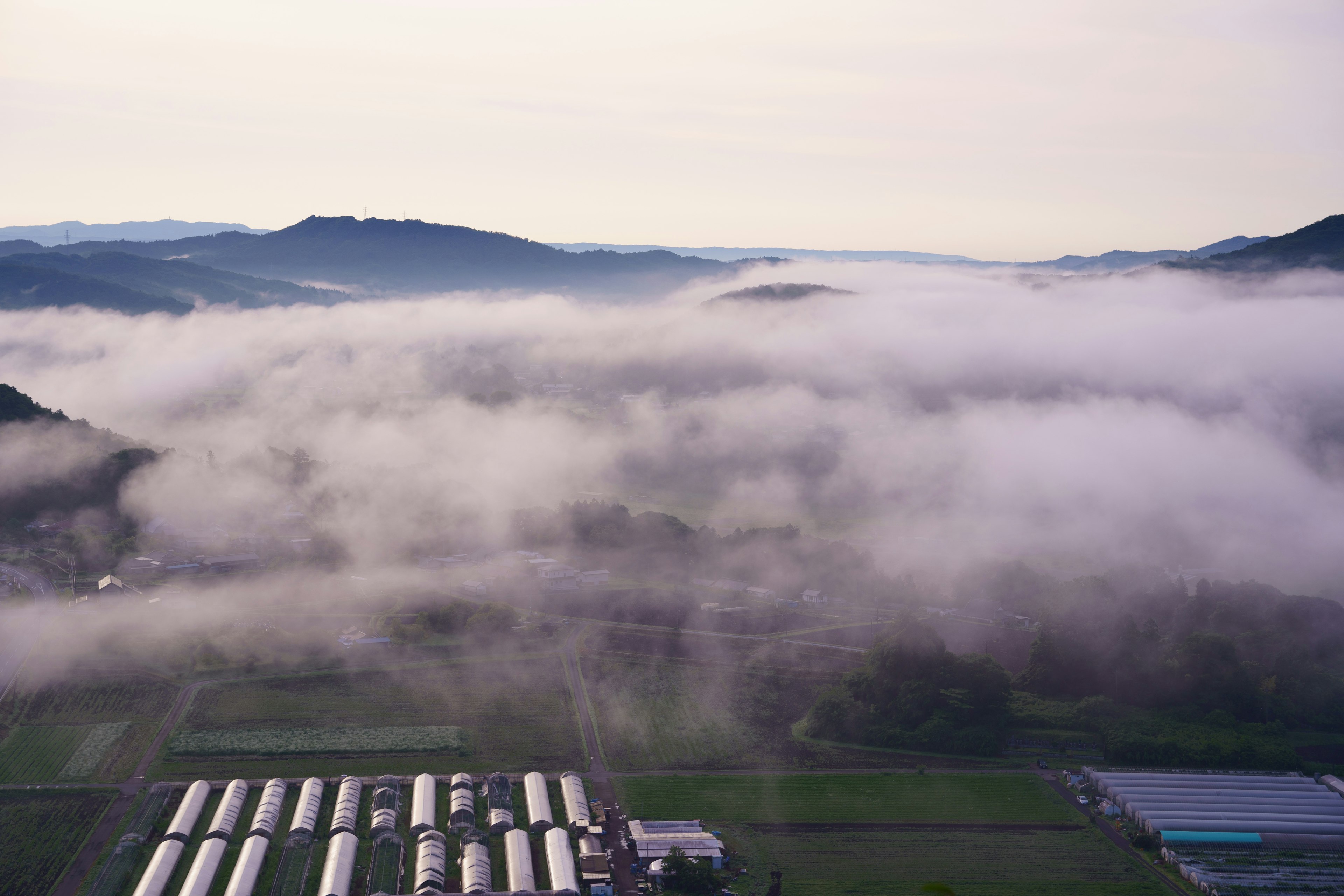 Paesaggio coperto di nebbia circondato da montagne con strutture agricole