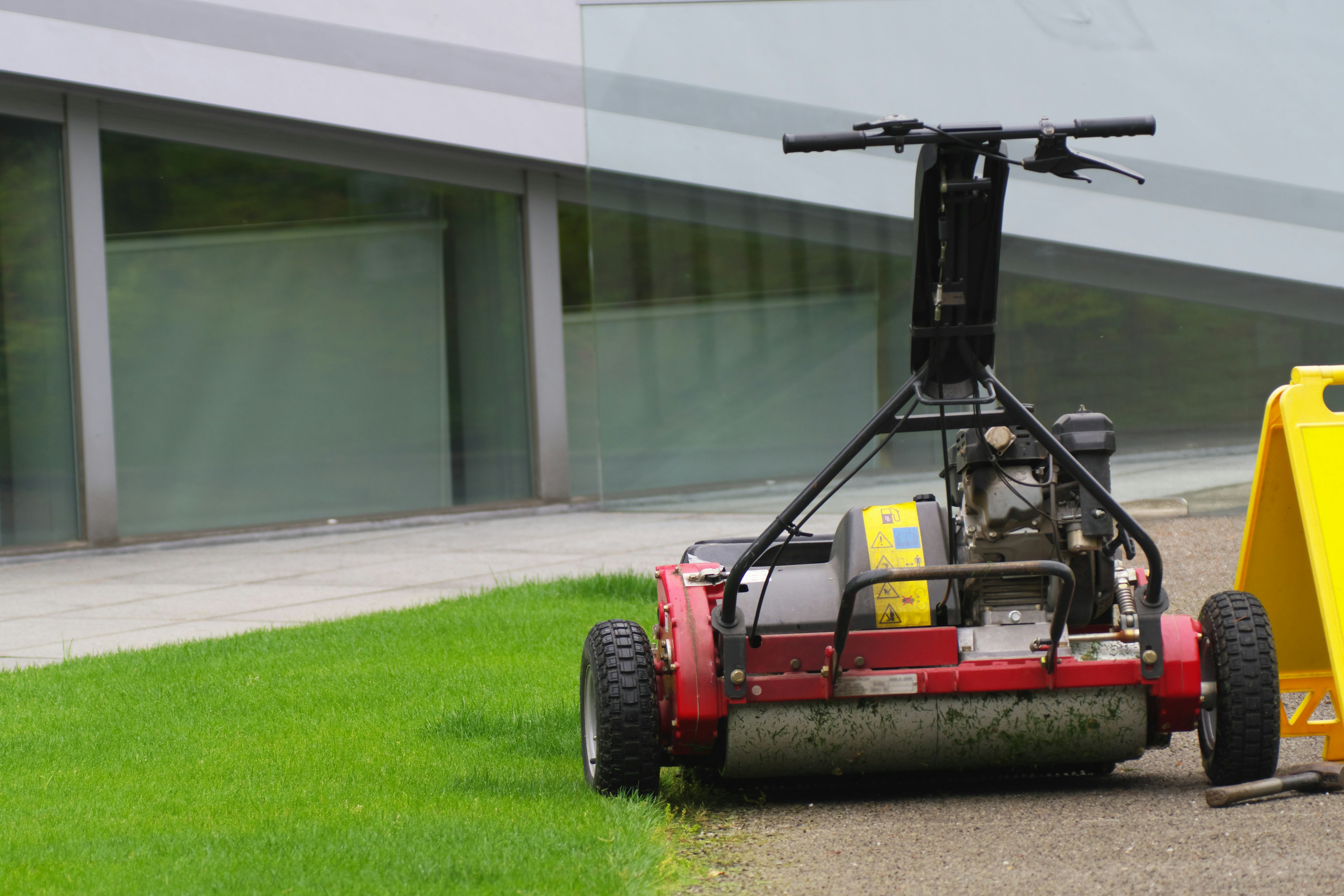 Red lawn mower positioned on grass near a modern building