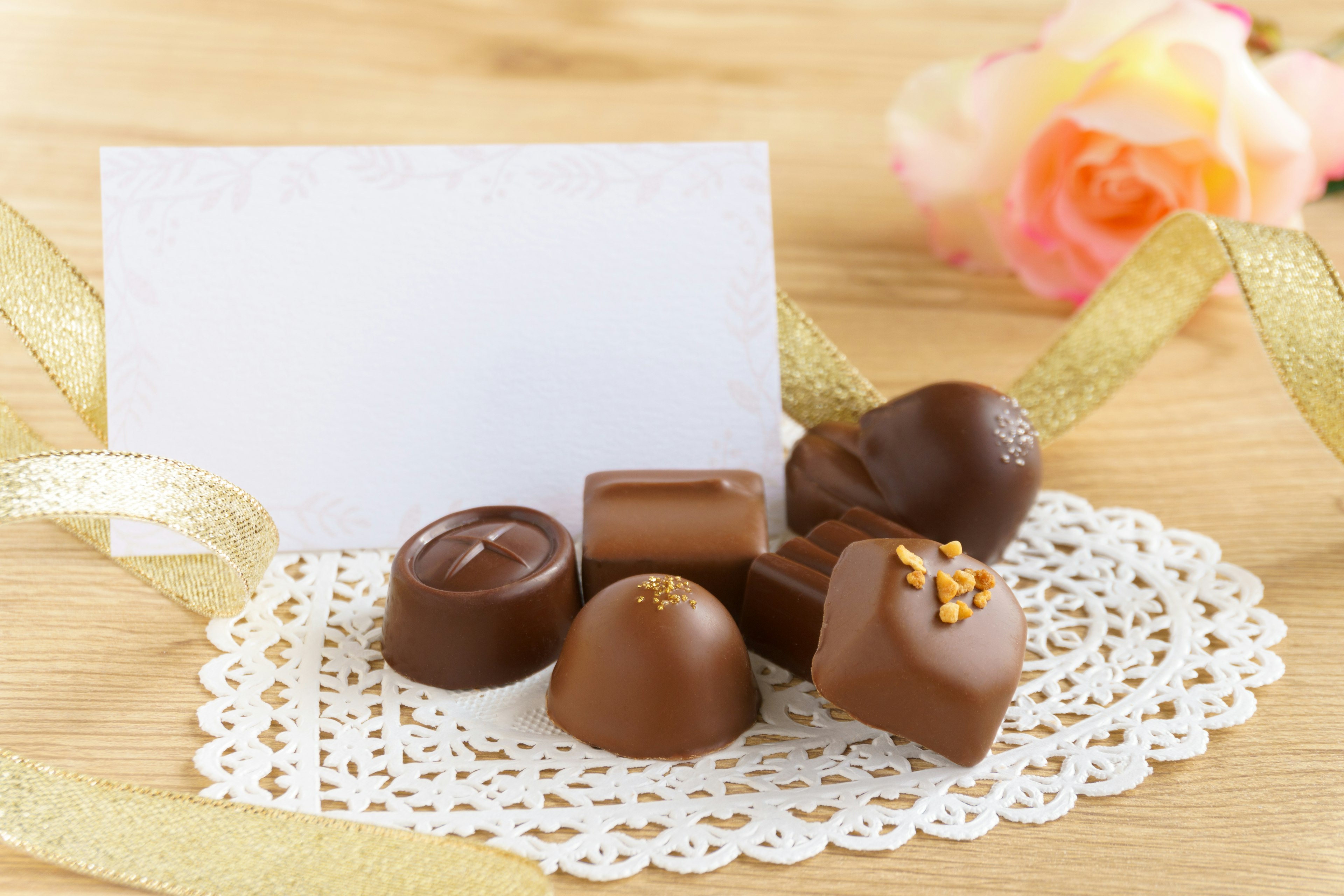 Cioccolatini assortiti su un centrino di pizzo con una cartolina bianca e una rosa rosa