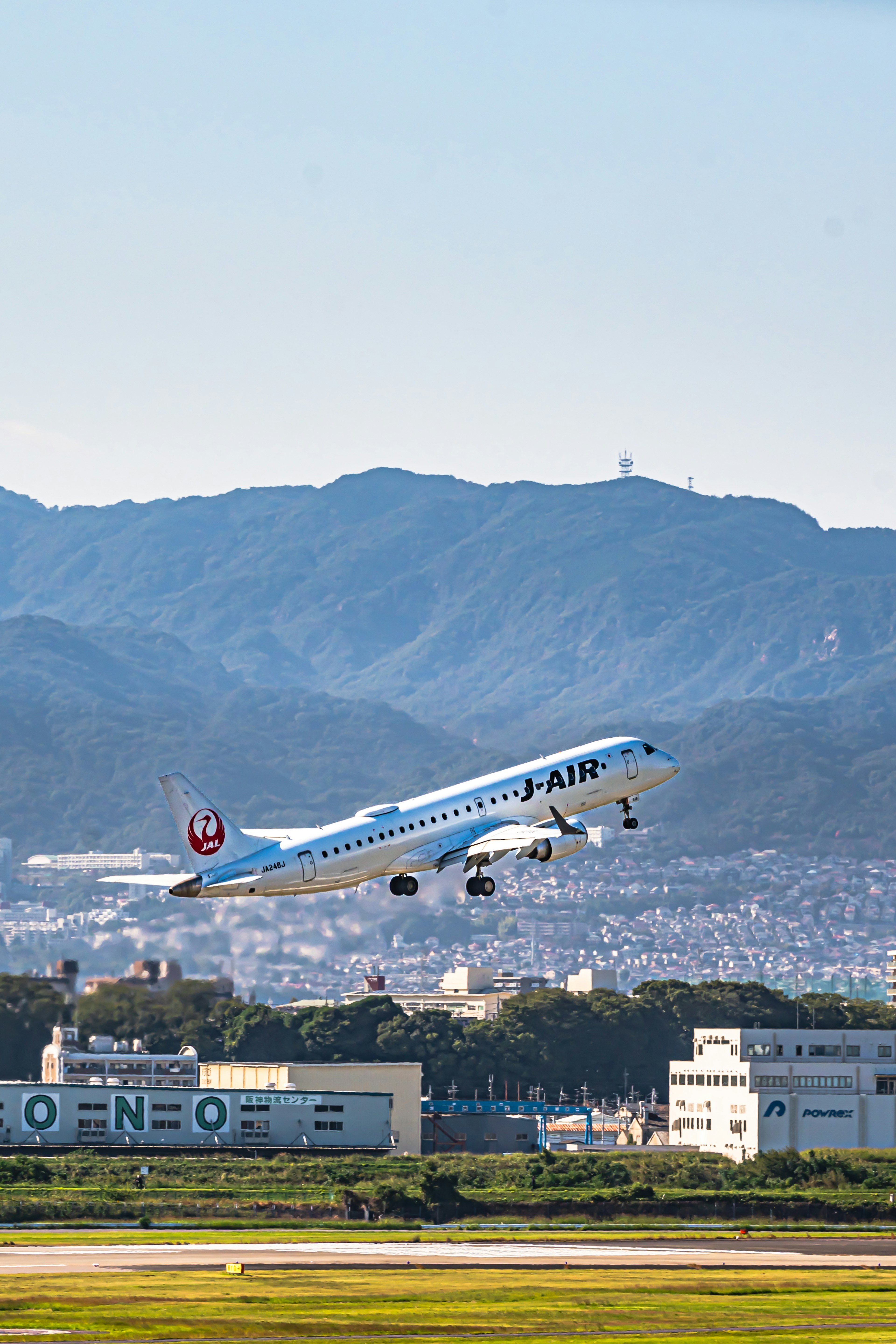 青い飛行機が空に向かって上昇している風景 背景には山と都市の風景