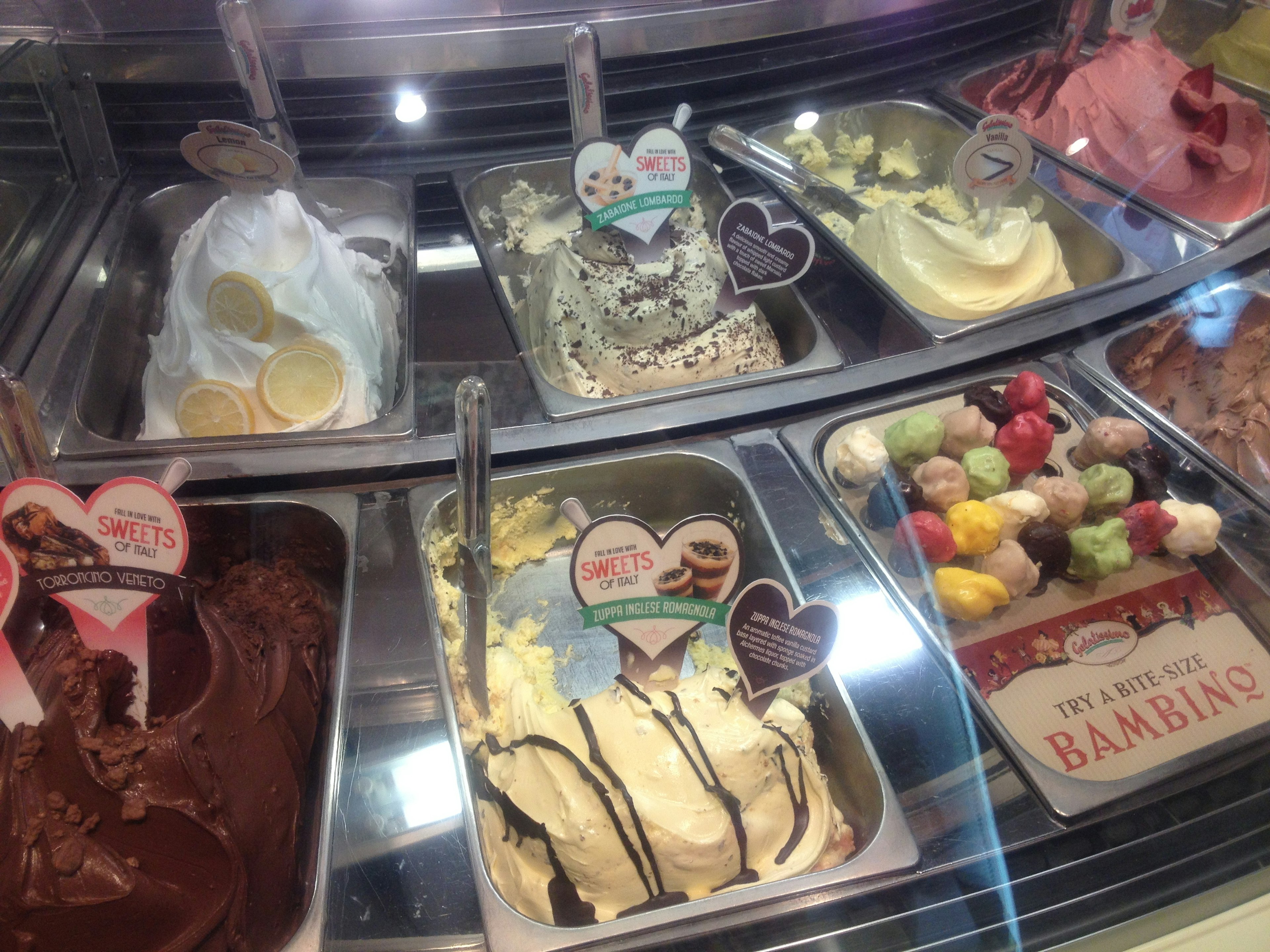 Varietà di gusti di gelato e di guarnizioni esposte in una vetrina