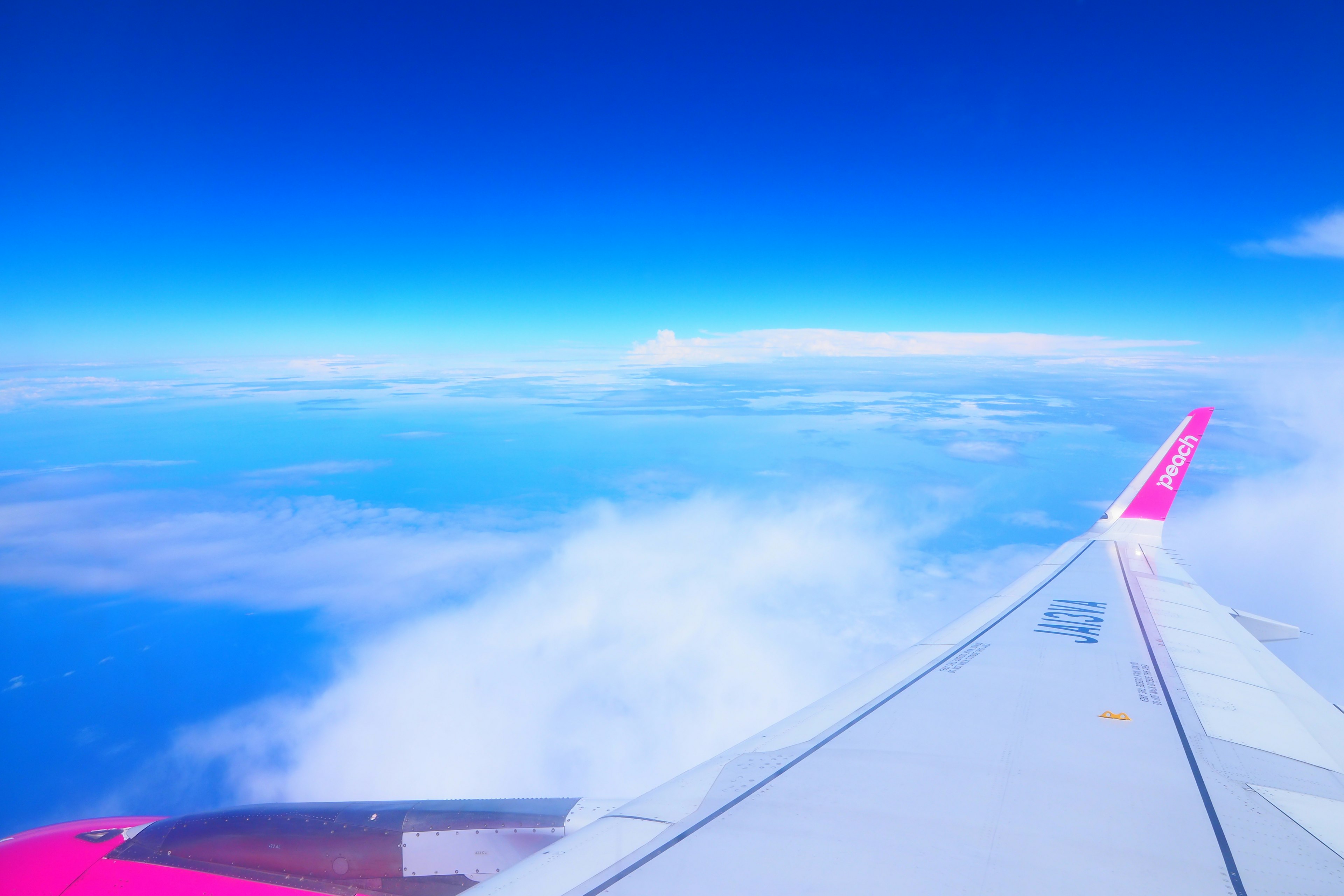 Airplane wing against a bright blue sky with clouds