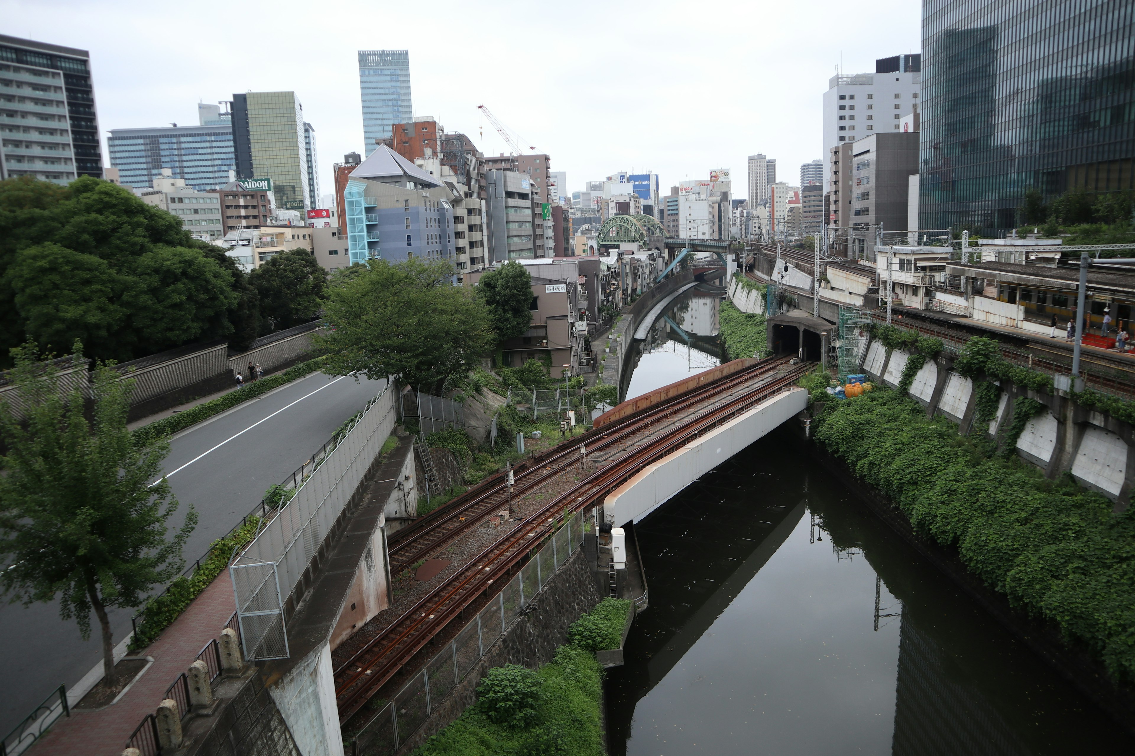 ทิวทัศน์เมืองที่มีแม่น้ำและทางรถไฟตัดกัน มีตึกระฟ้าอยู่เบื้องหลัง