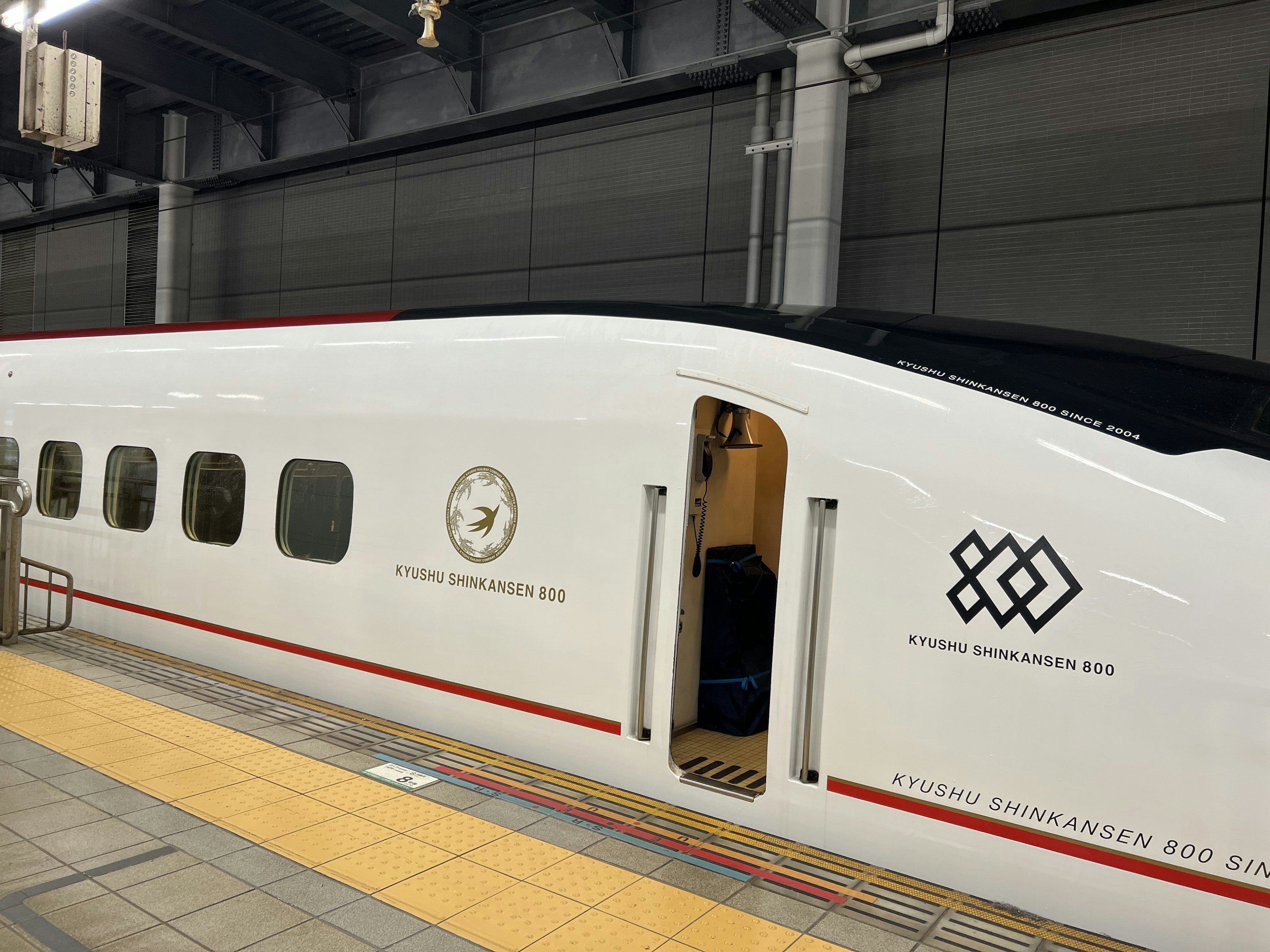 Tàu Shinkansen màu trắng tại nhà ga với logo đặc trưng