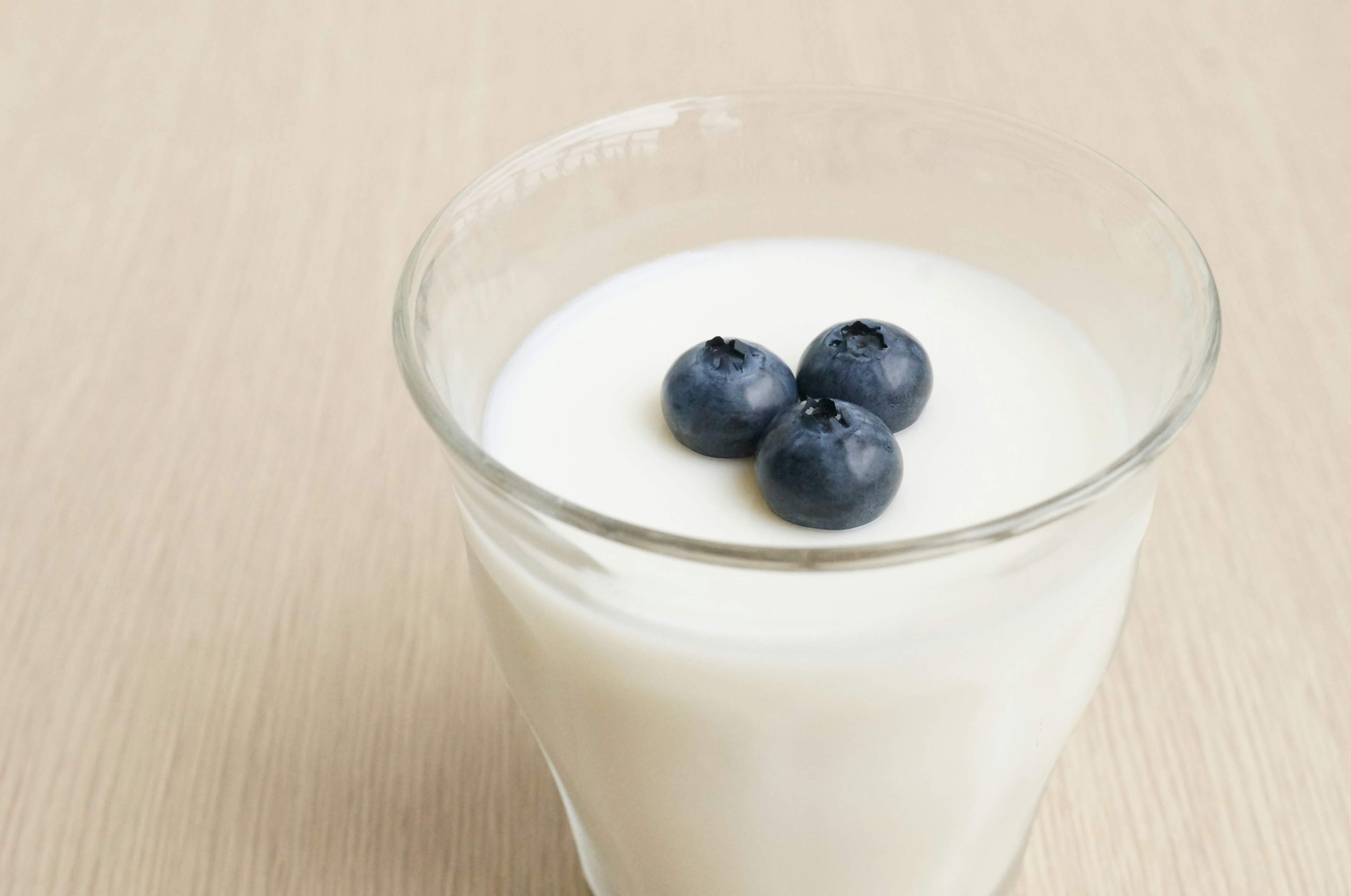 A glass of yogurt topped with blueberries on a light-colored surface