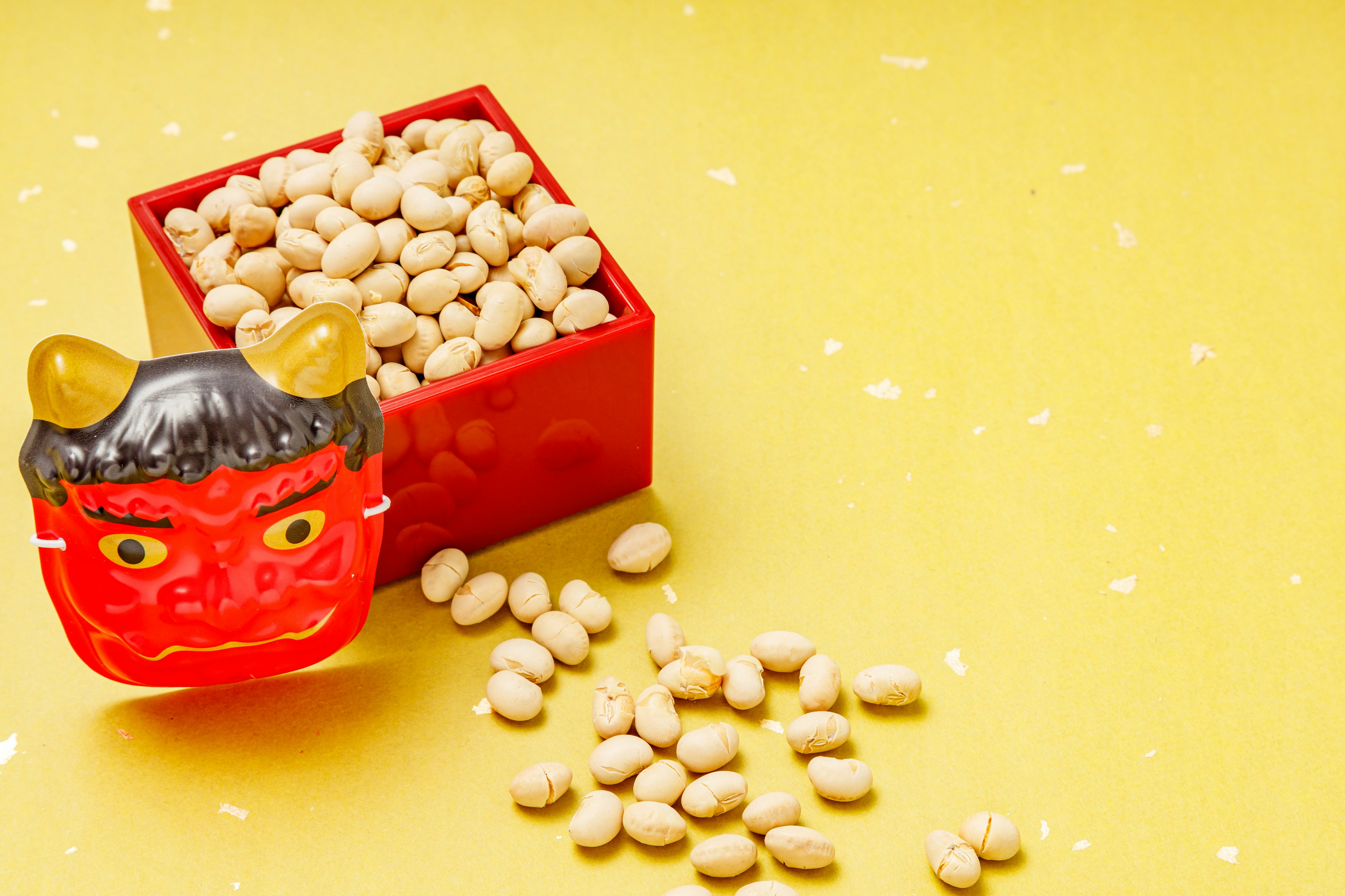 Red box filled with beans and a traditional demon mask on a yellow background