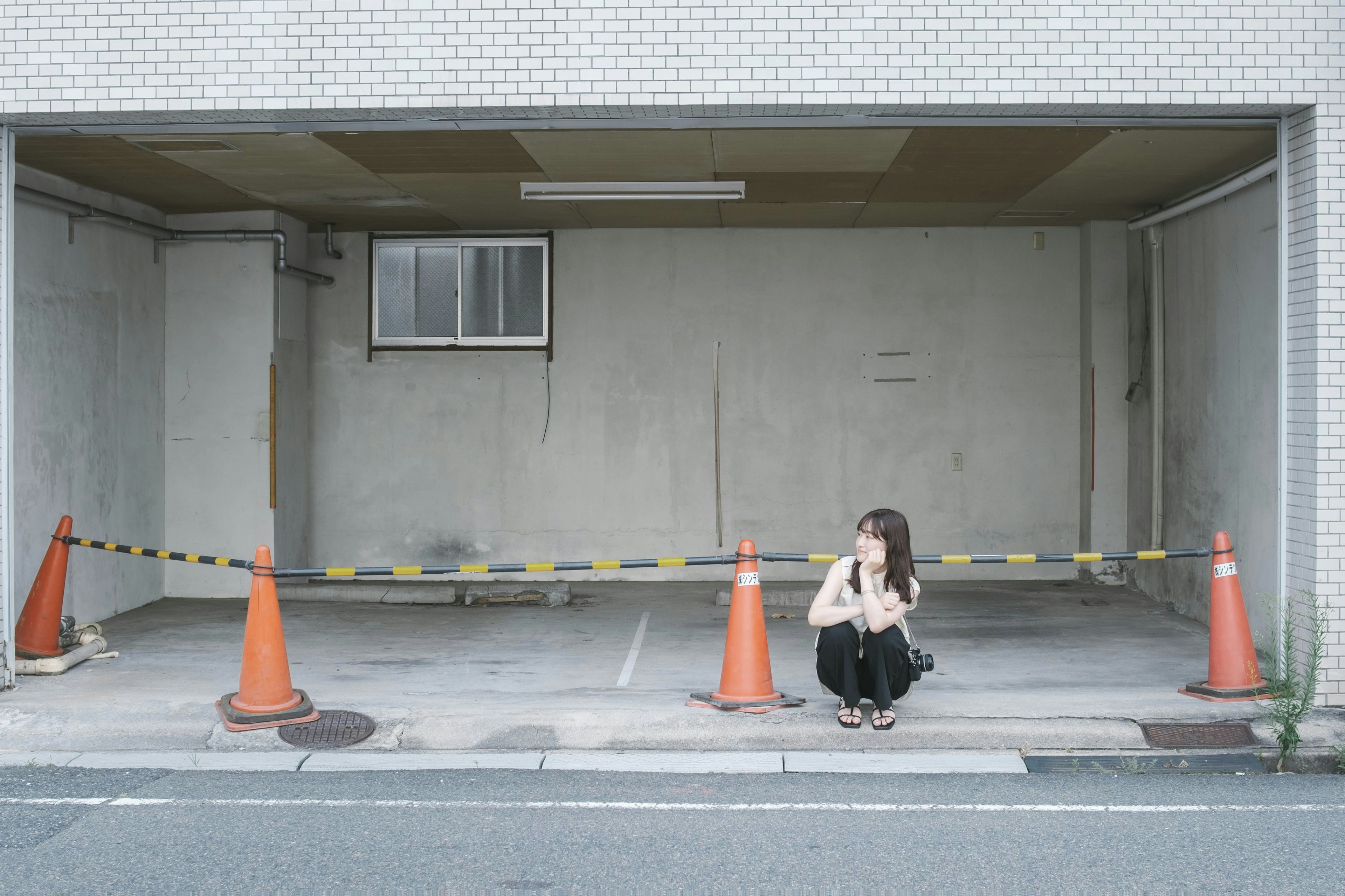 空の駐車場に座る女性とオレンジのコーン