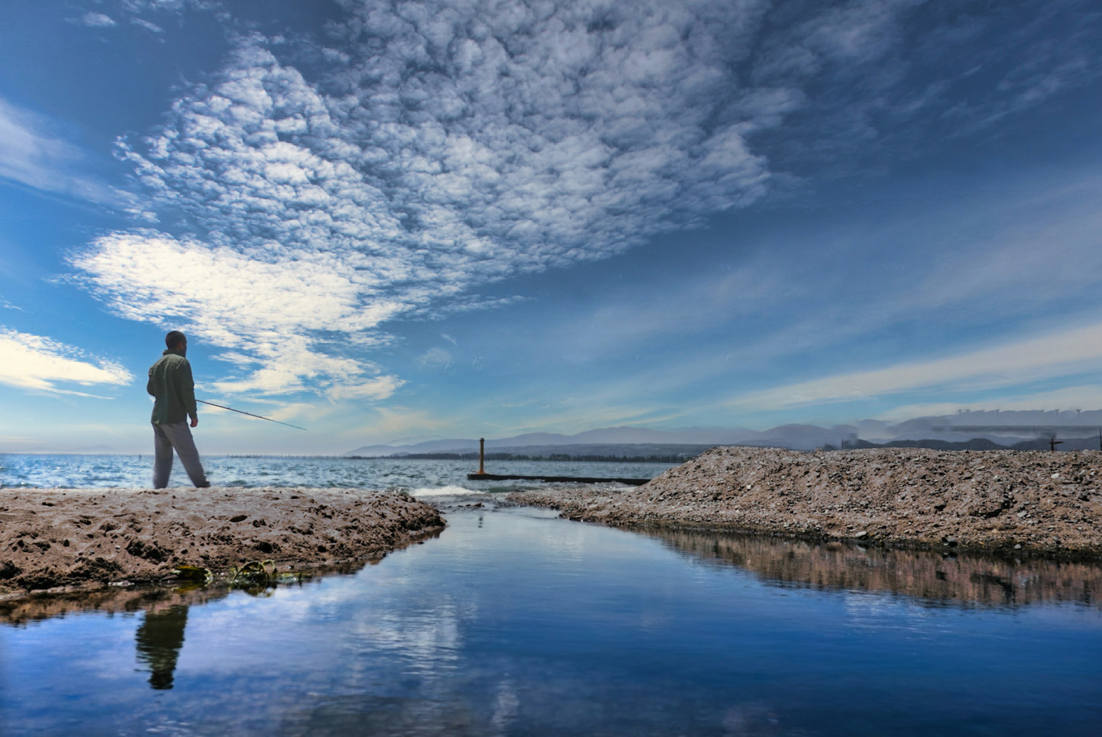 Une personne debout sur une plage tranquille avec un ciel bleu et des reflets dans l'eau