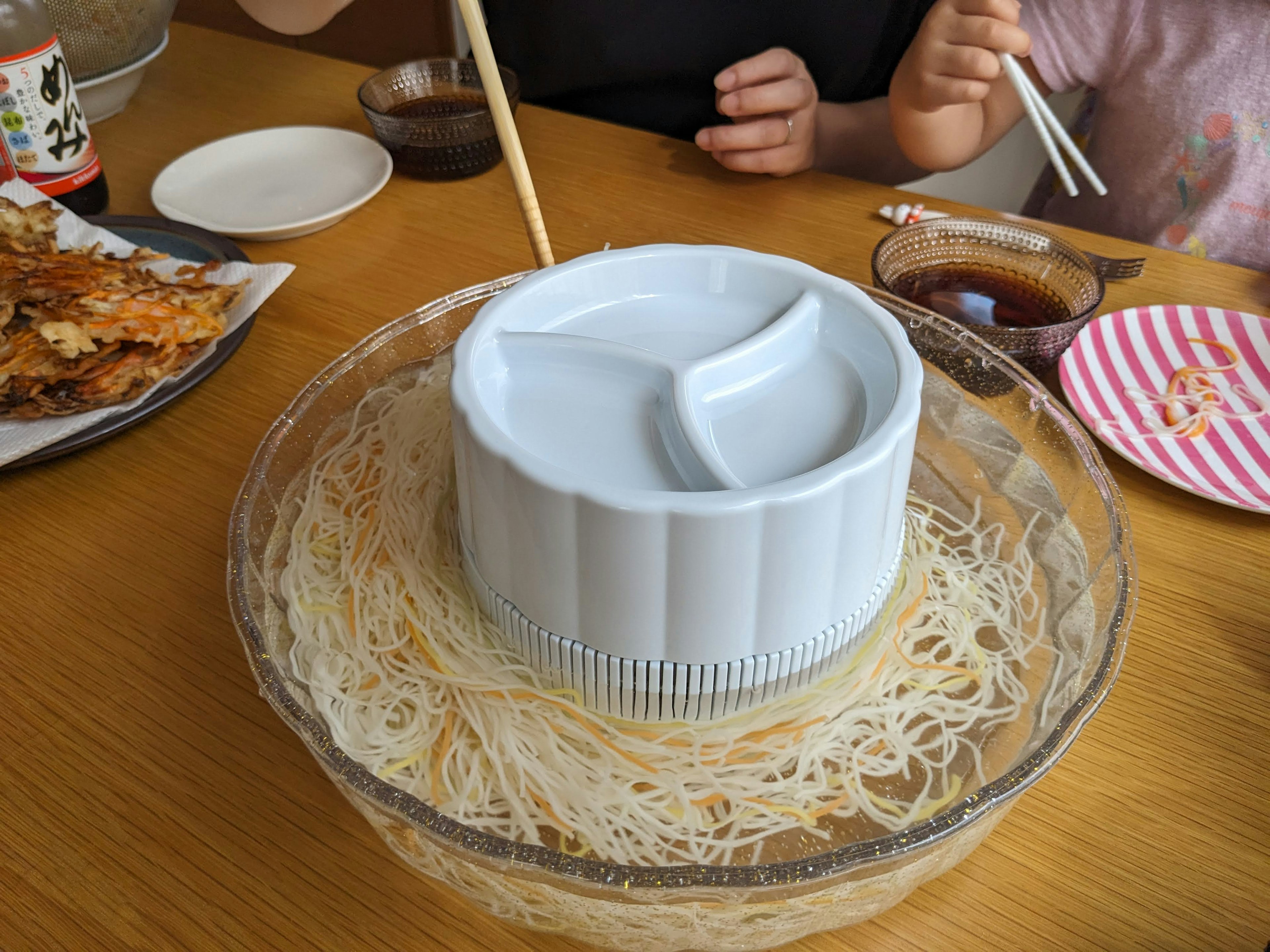 Plato blanco con fideos somen y palillos en una mesa con varios platos