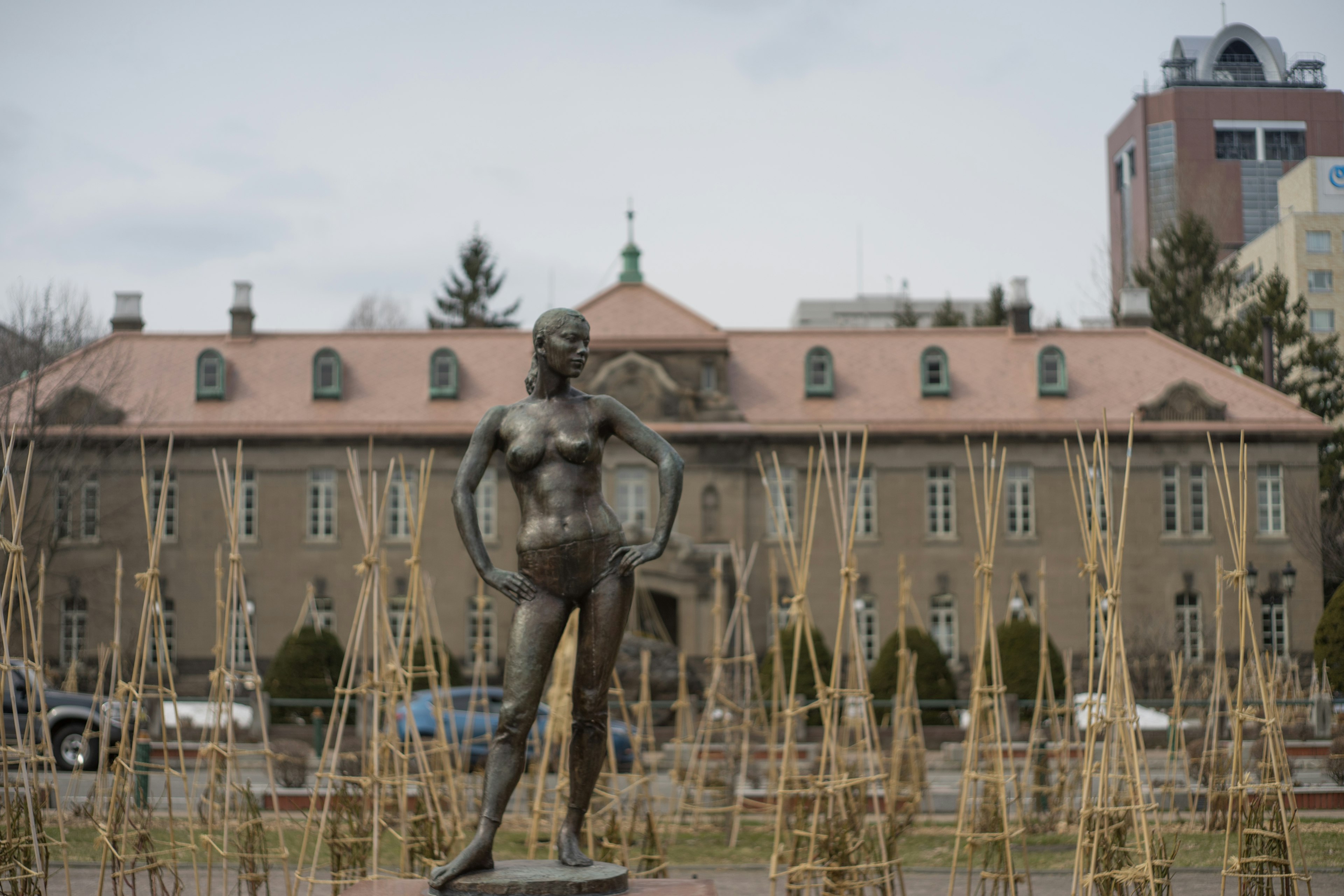 Una estatua de bronce de una mujer en un parque con un edificio histórico al fondo