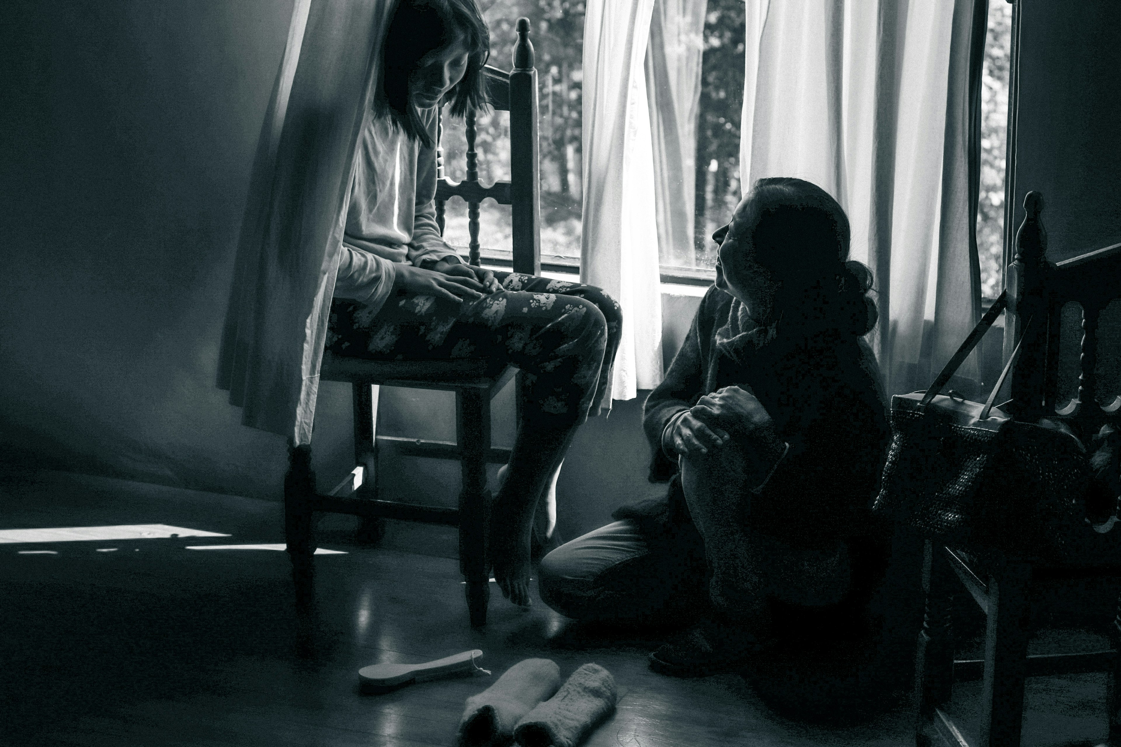 Photo en noir et blanc d'une fille assise sur une chaise et d'un garçon assis sur le sol dans une pièce calme