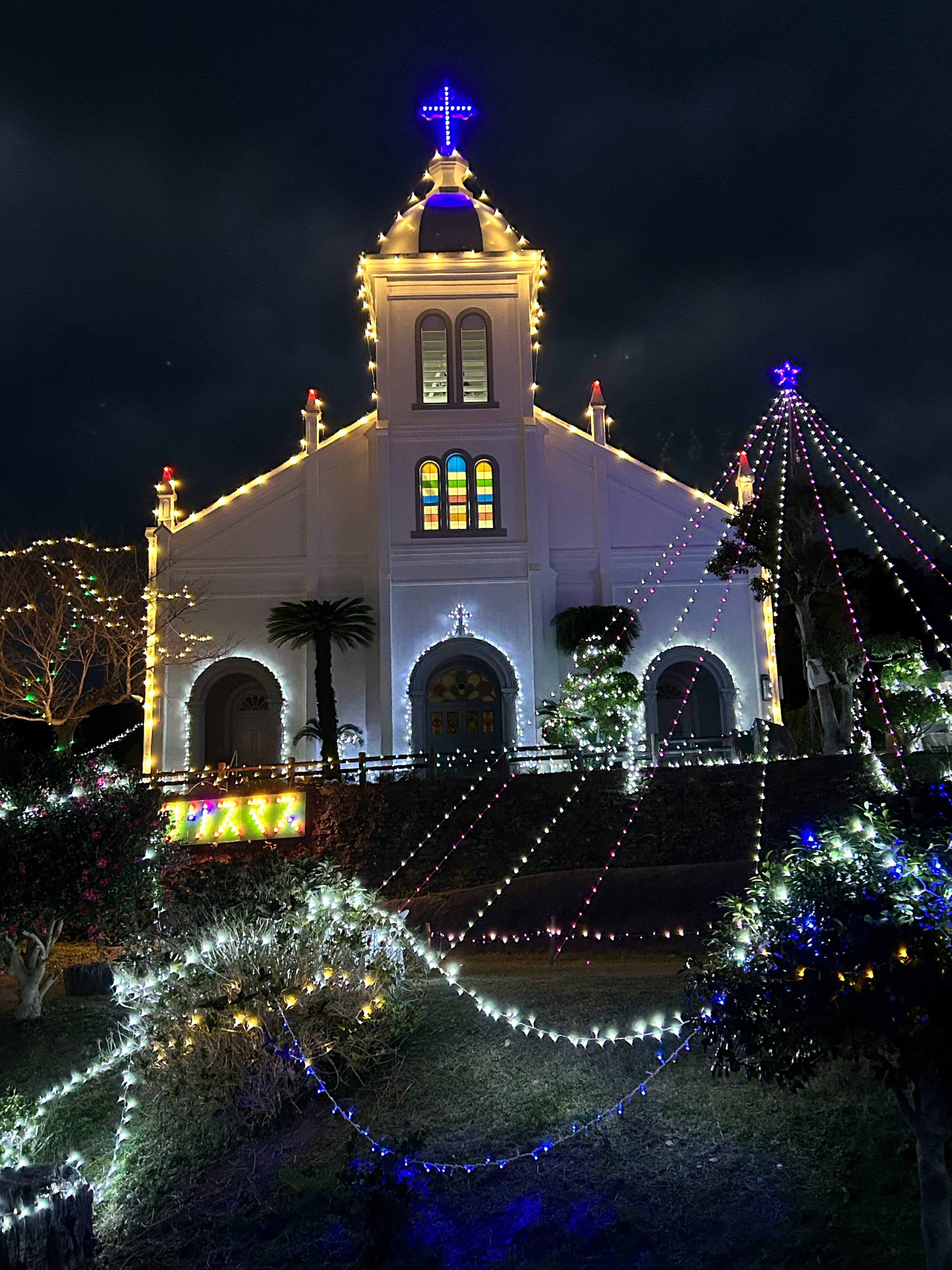 Fachada de iglesia blanca iluminada decorada con luces coloridas por la noche