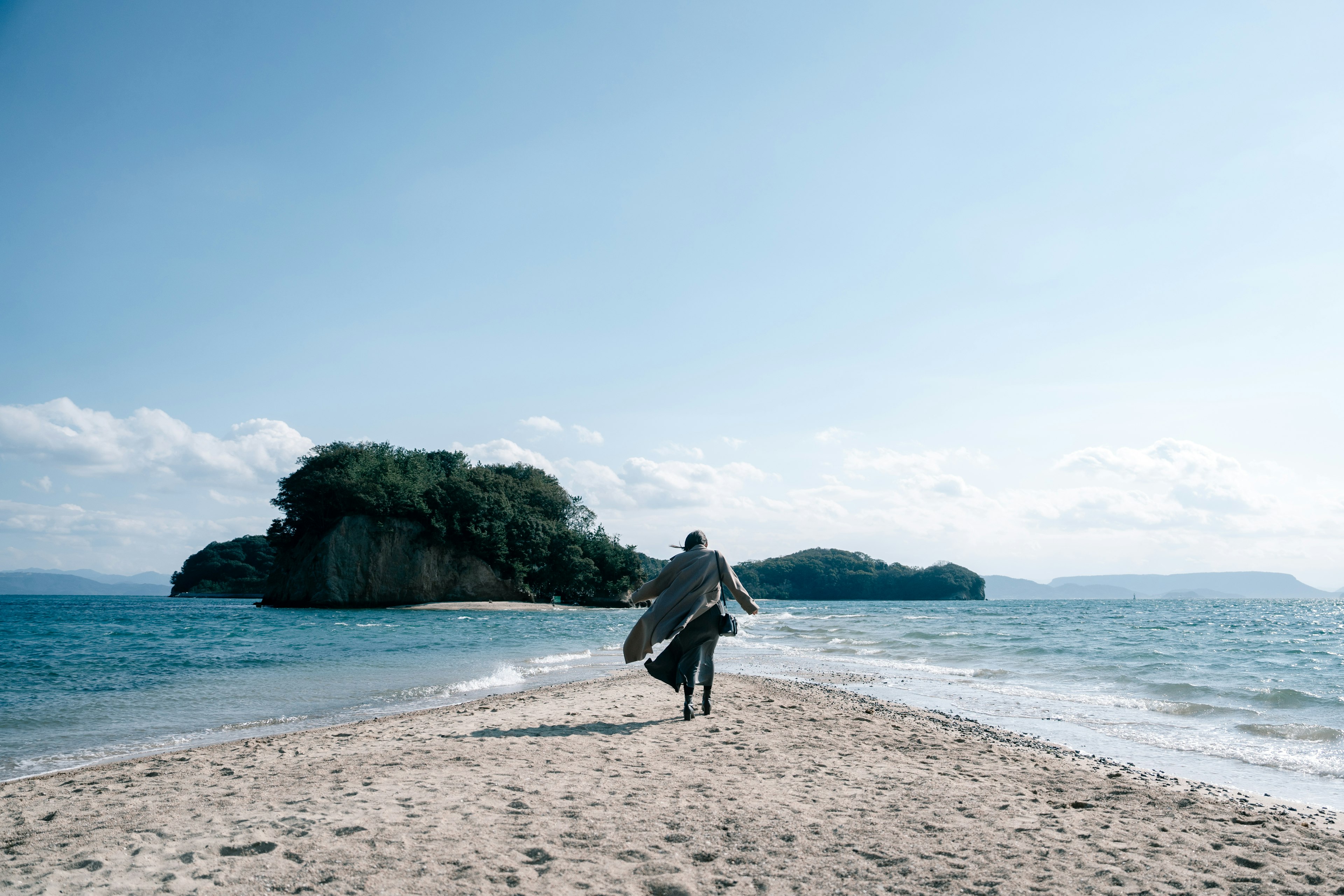 Persona che cammina sulla spiaggia con una tavola da surf e cielo blu